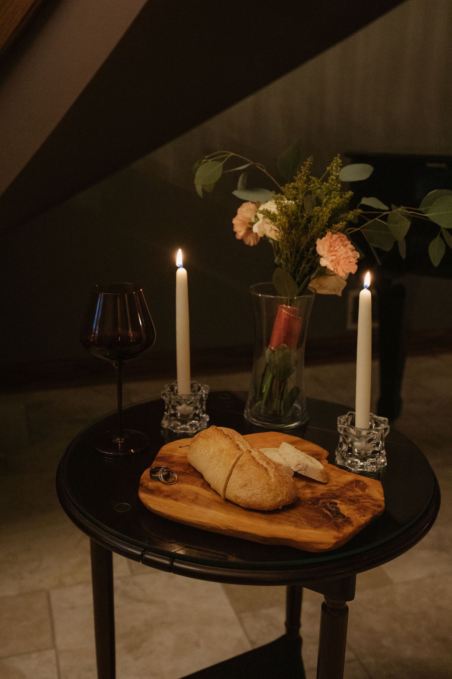 Romantic table setting with candles, flowers and bread on a dark wooden surface.