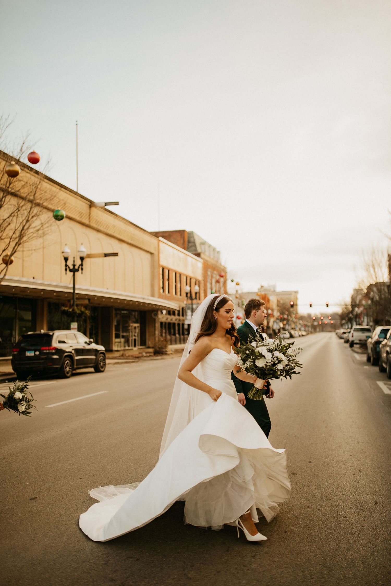 A couple in wedding attire running playfully down an empty small-town street at sunset.