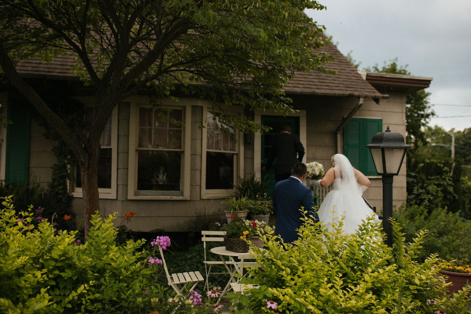 A couple stands outside a charming craftsman-style house with lush yellow-green landscaping.
