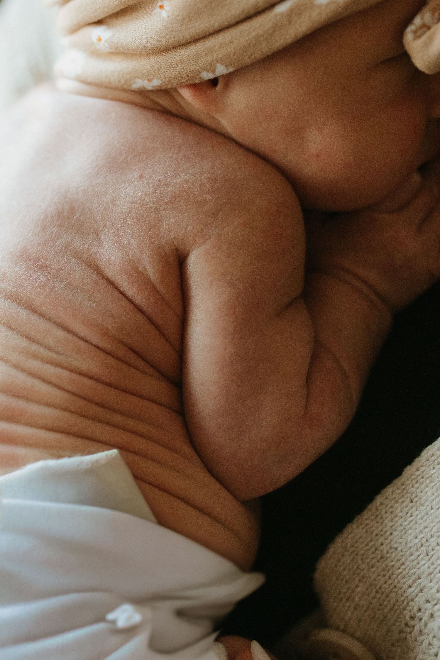 Artistic close-up of newborn baby's arm and torso wrapped in soft white fabric.
