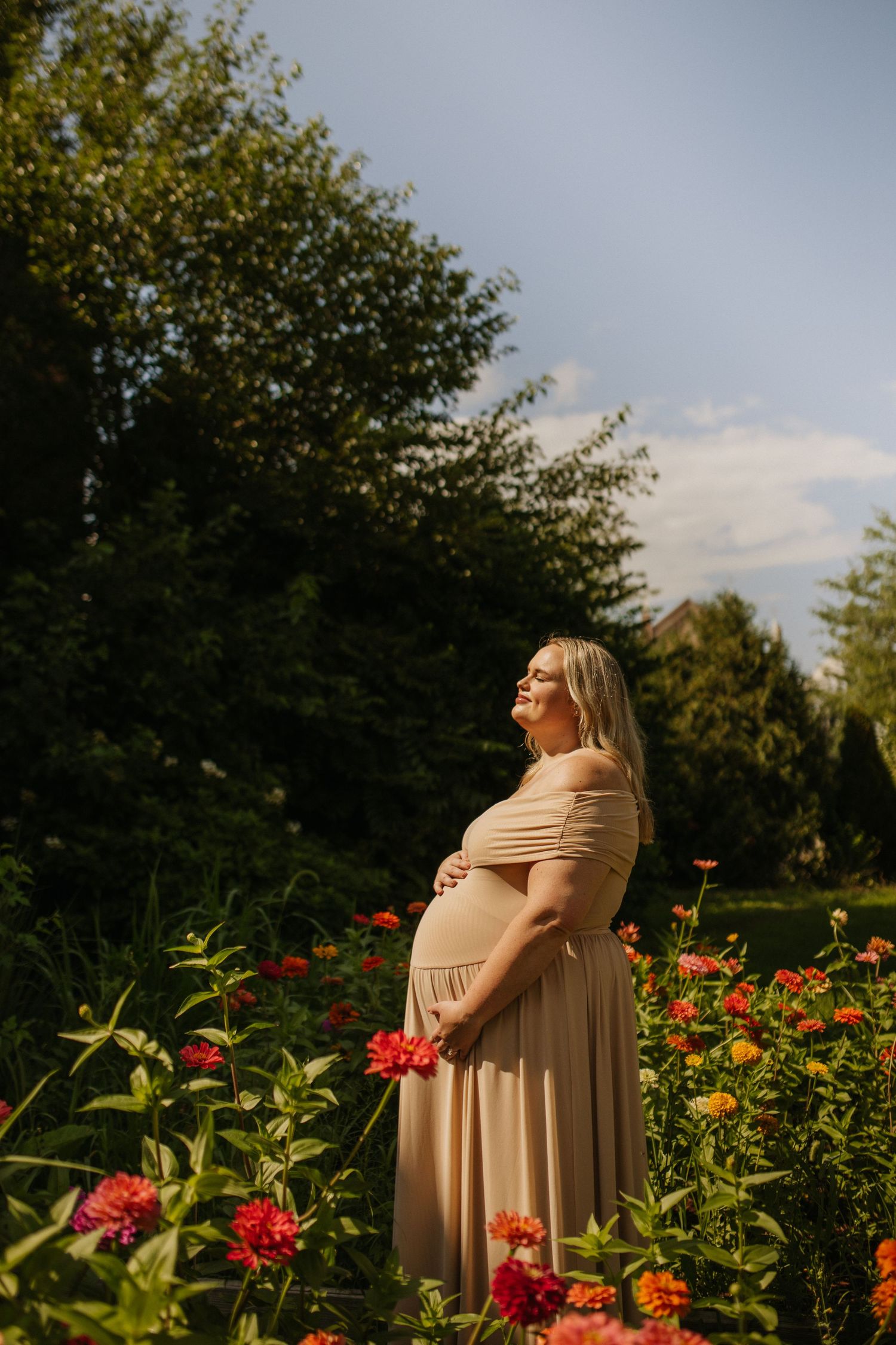 Radiant maternity portrait in garden with vibrant zinnias and natural sunlight.
