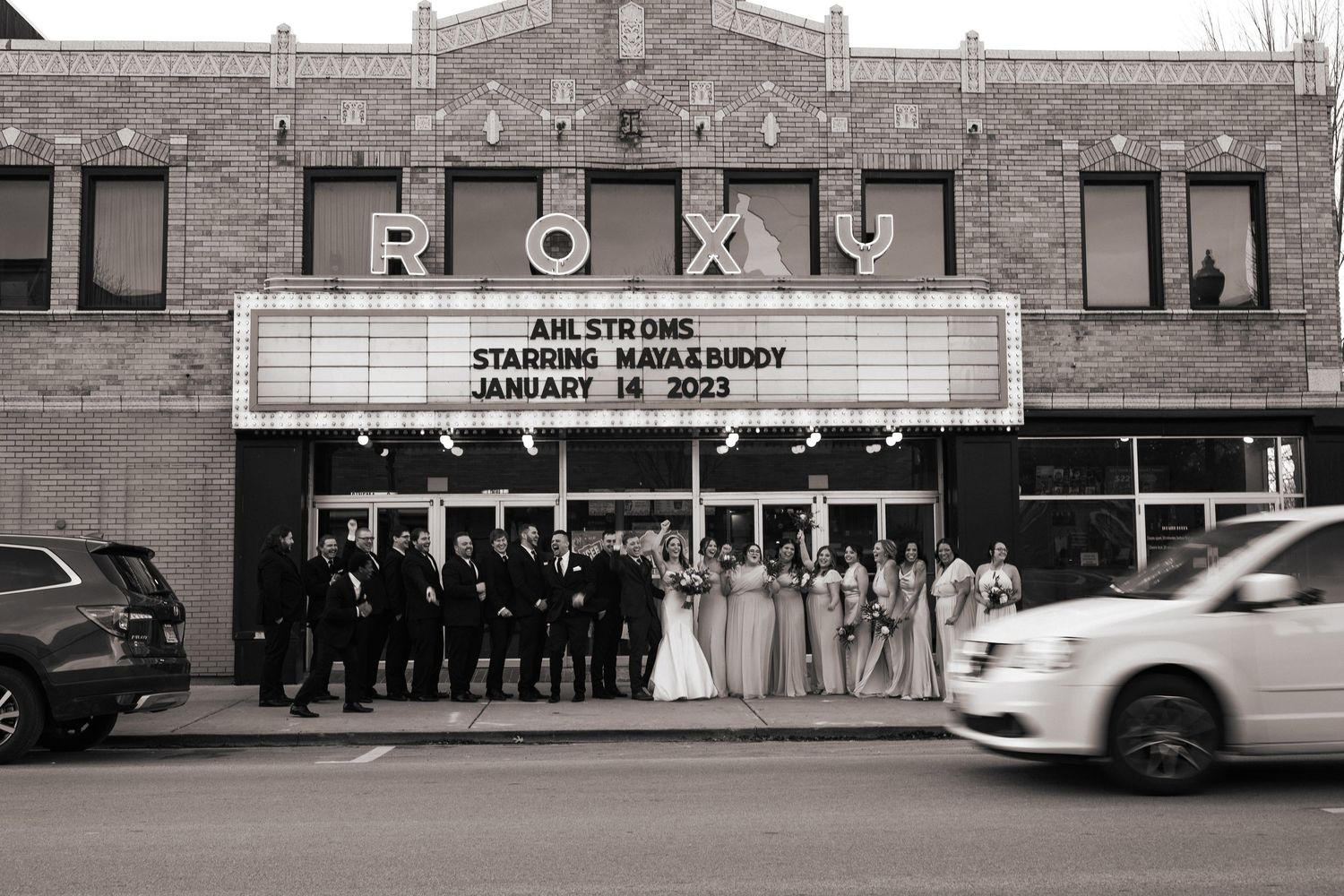 A wedding party poses in front of a vintage theater marquee displaying their wedding date.