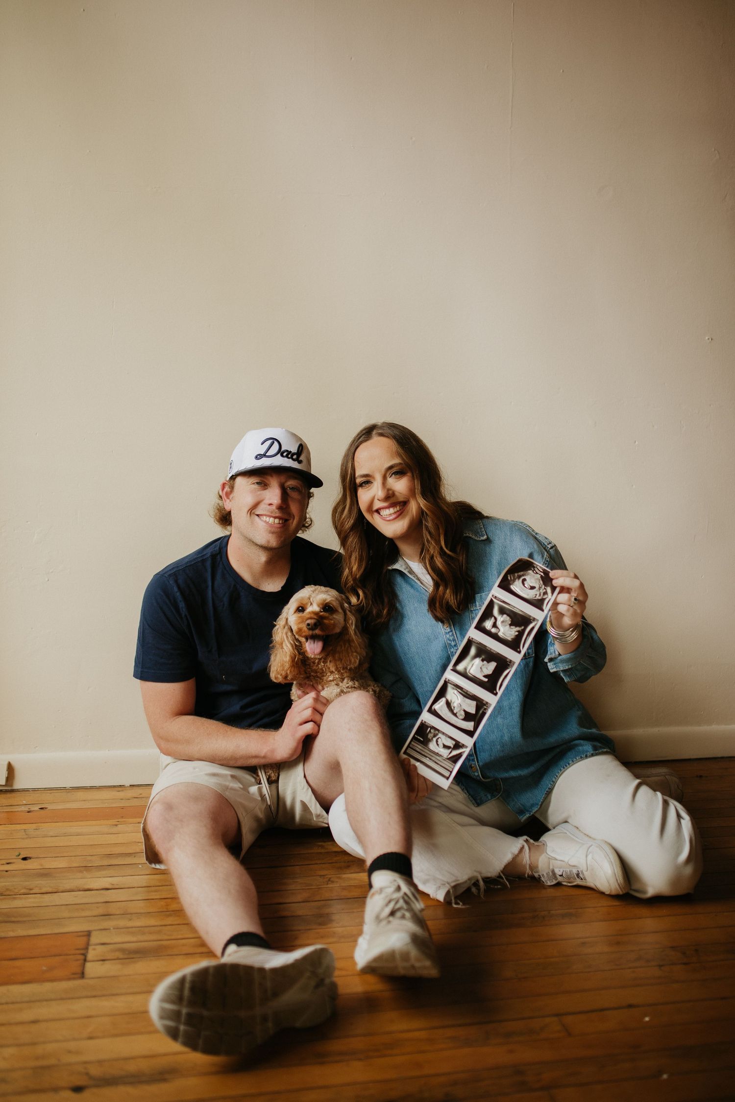 Couple sitting on wooden floor holding small chalkboard signs for pregnancy announcement.