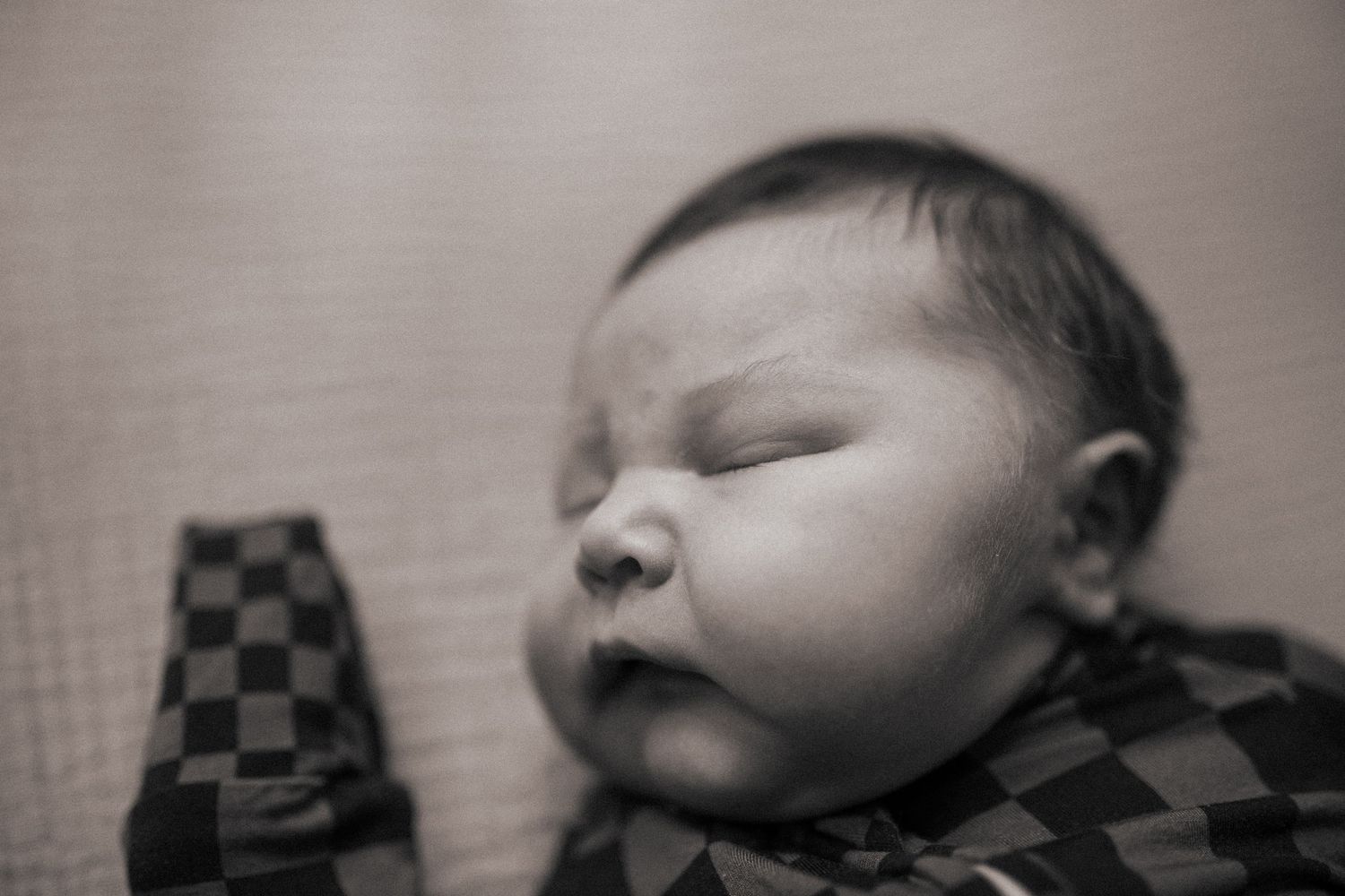 Close-up black and white view of a sleeping baby wearing checkered clothing.