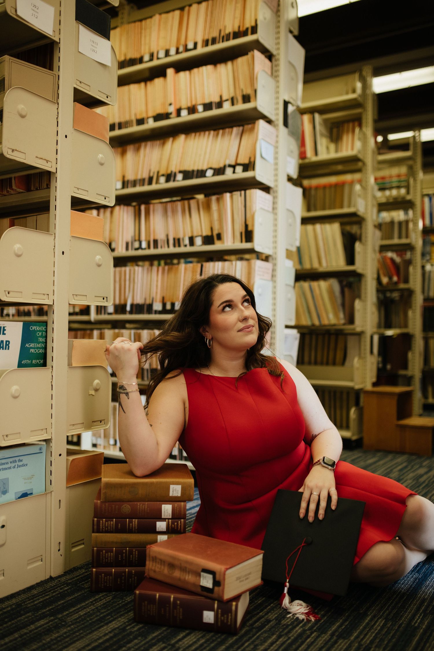 A person in red poses among library bookshelves filled with academic materials.