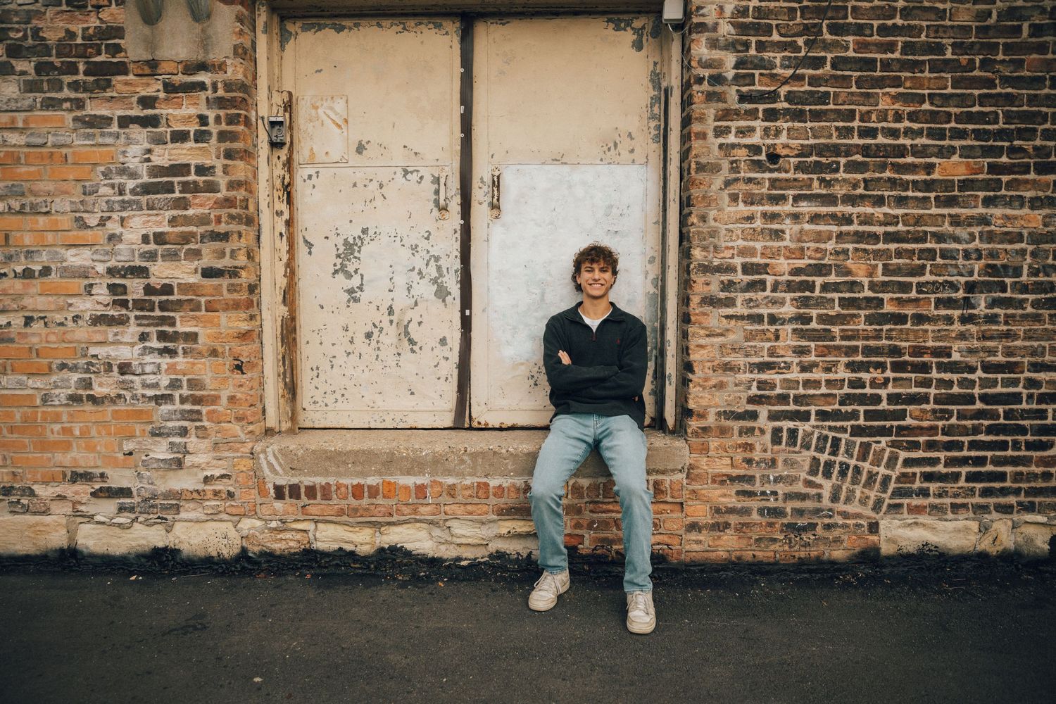 A casual portrait against a weathered brick wall with a white door.