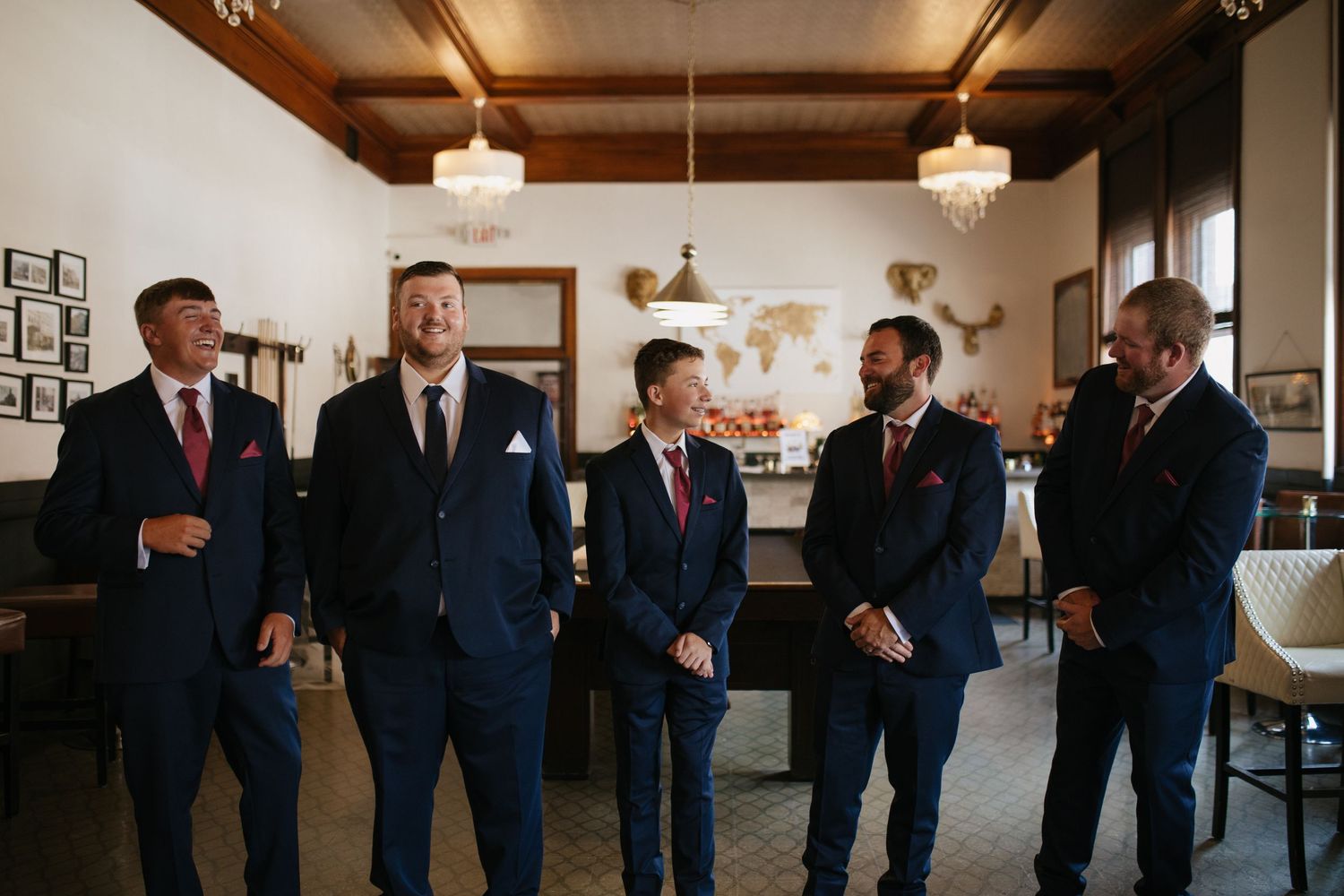 Groomsmen in navy suits gather in elegant indoor venue before ceremony.