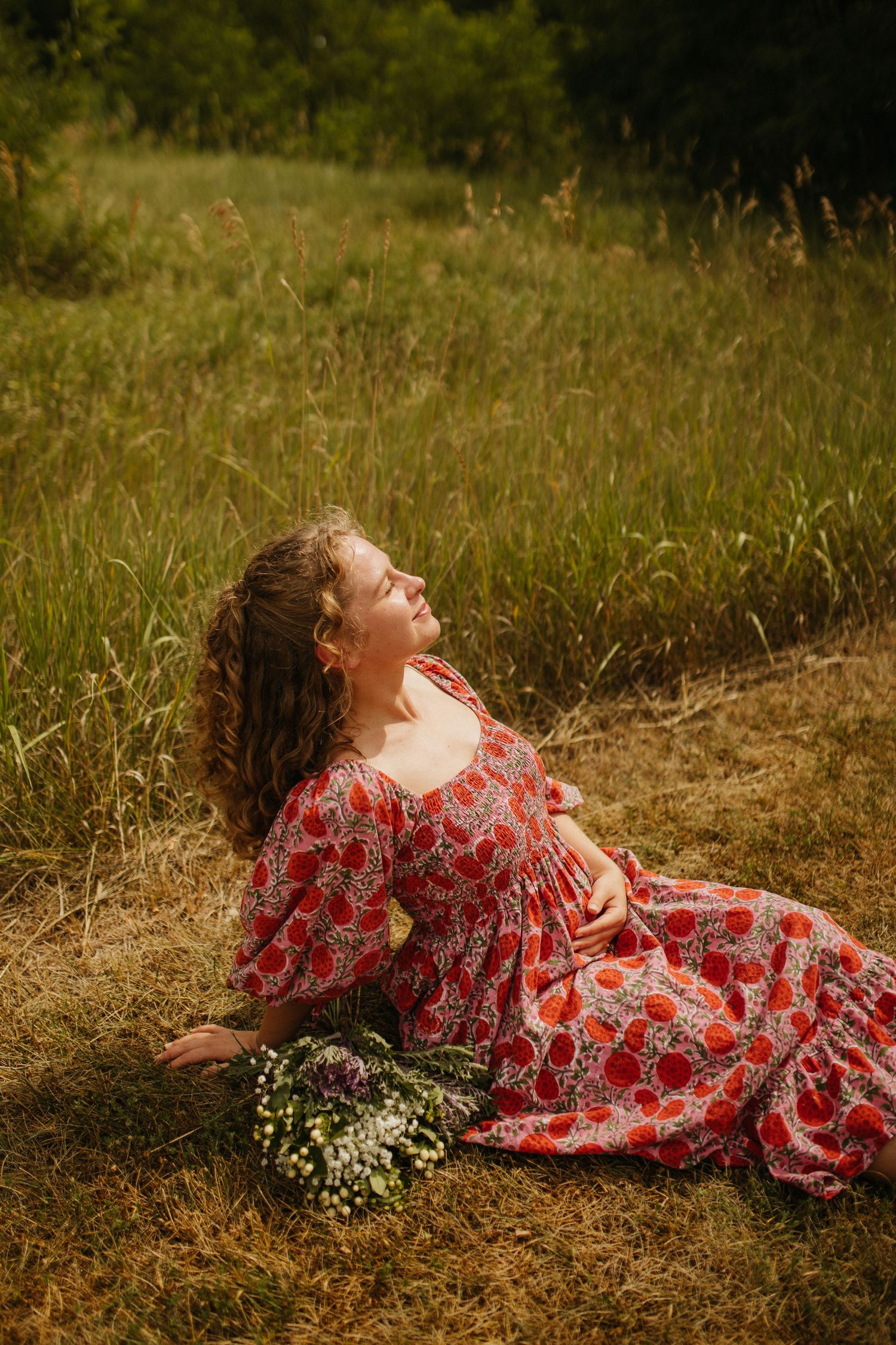 Person in red floral dress lying in tall grass field during sunset.