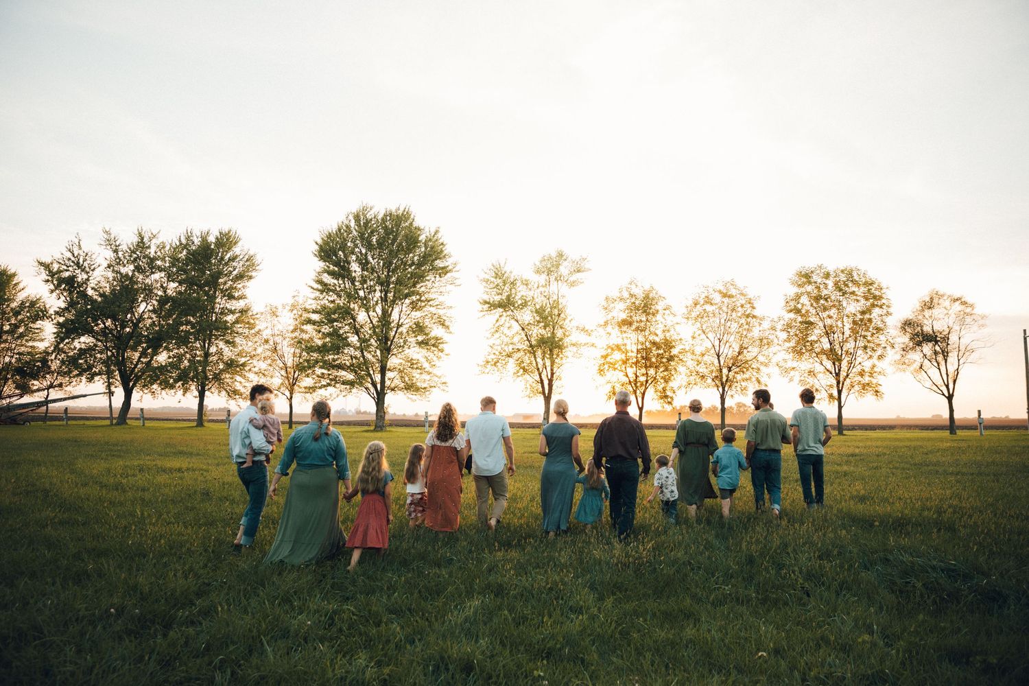Group of people standing in a line against a sunset sky on a hilltop.