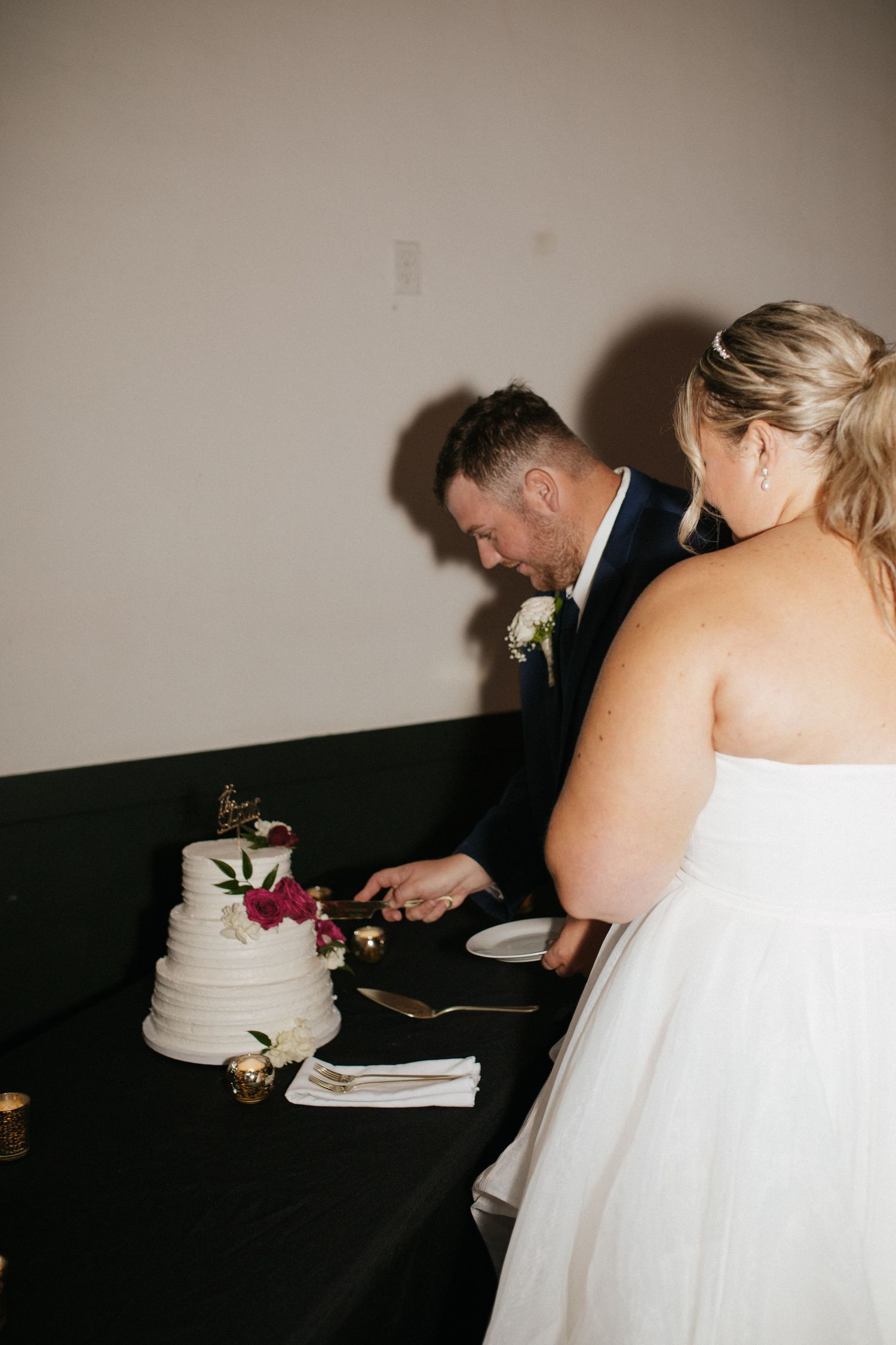 Elegant white wedding cake being cut on a dark table at a reception.