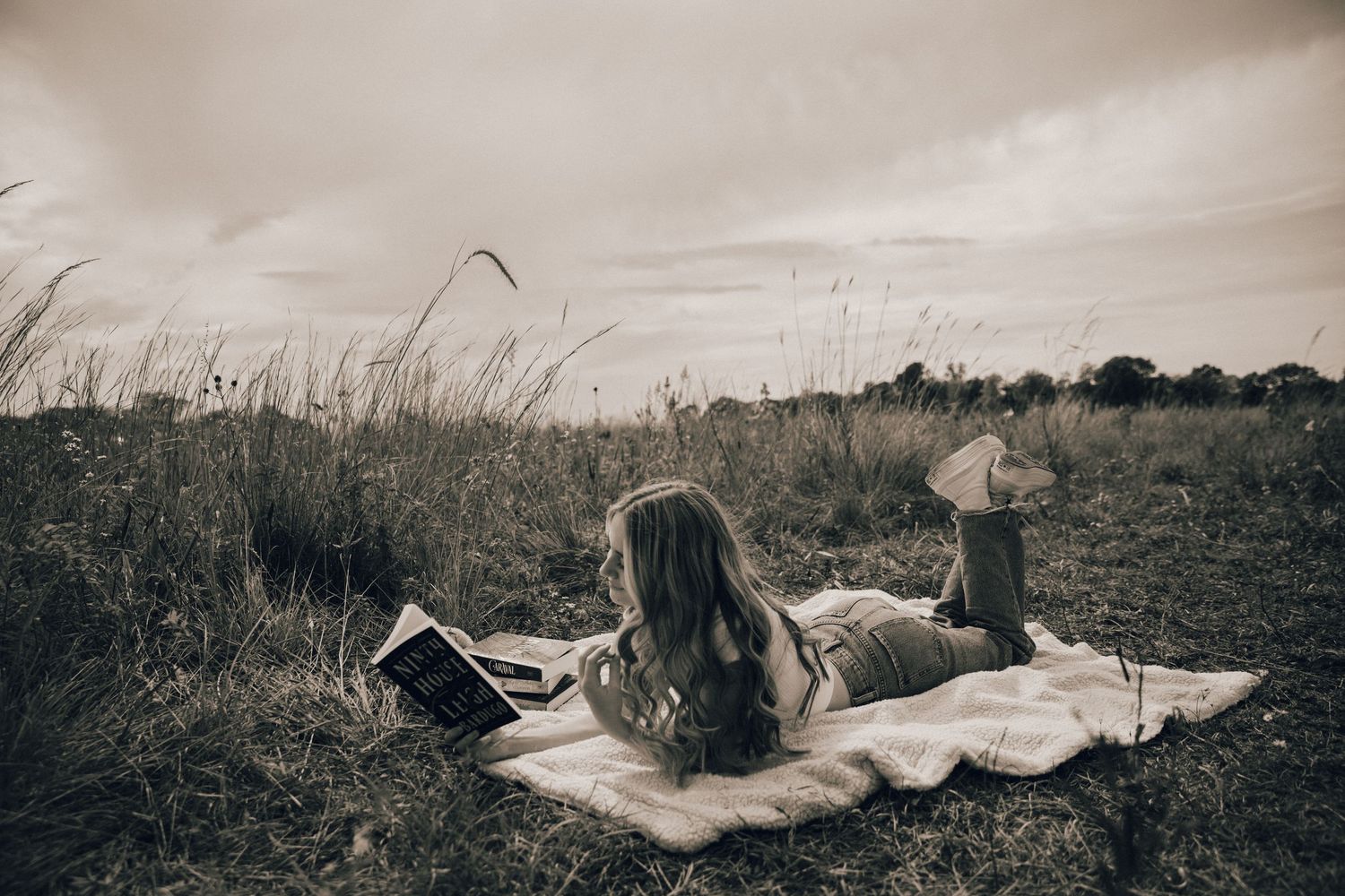 A black and white image of someone reading on a blanket in a meadow.