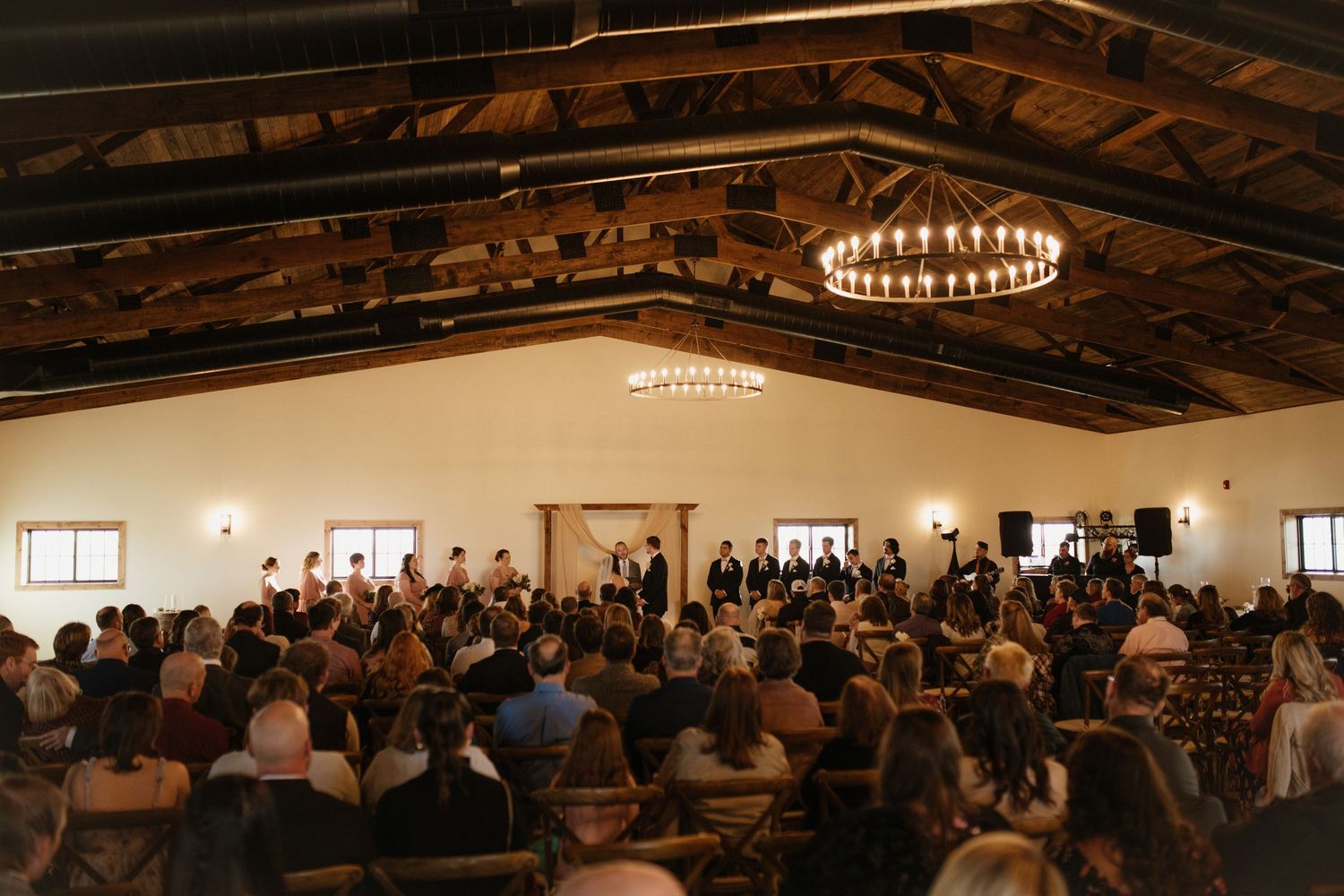 Wedding ceremony in a spacious venue with dramatic lighting and gathered guests.