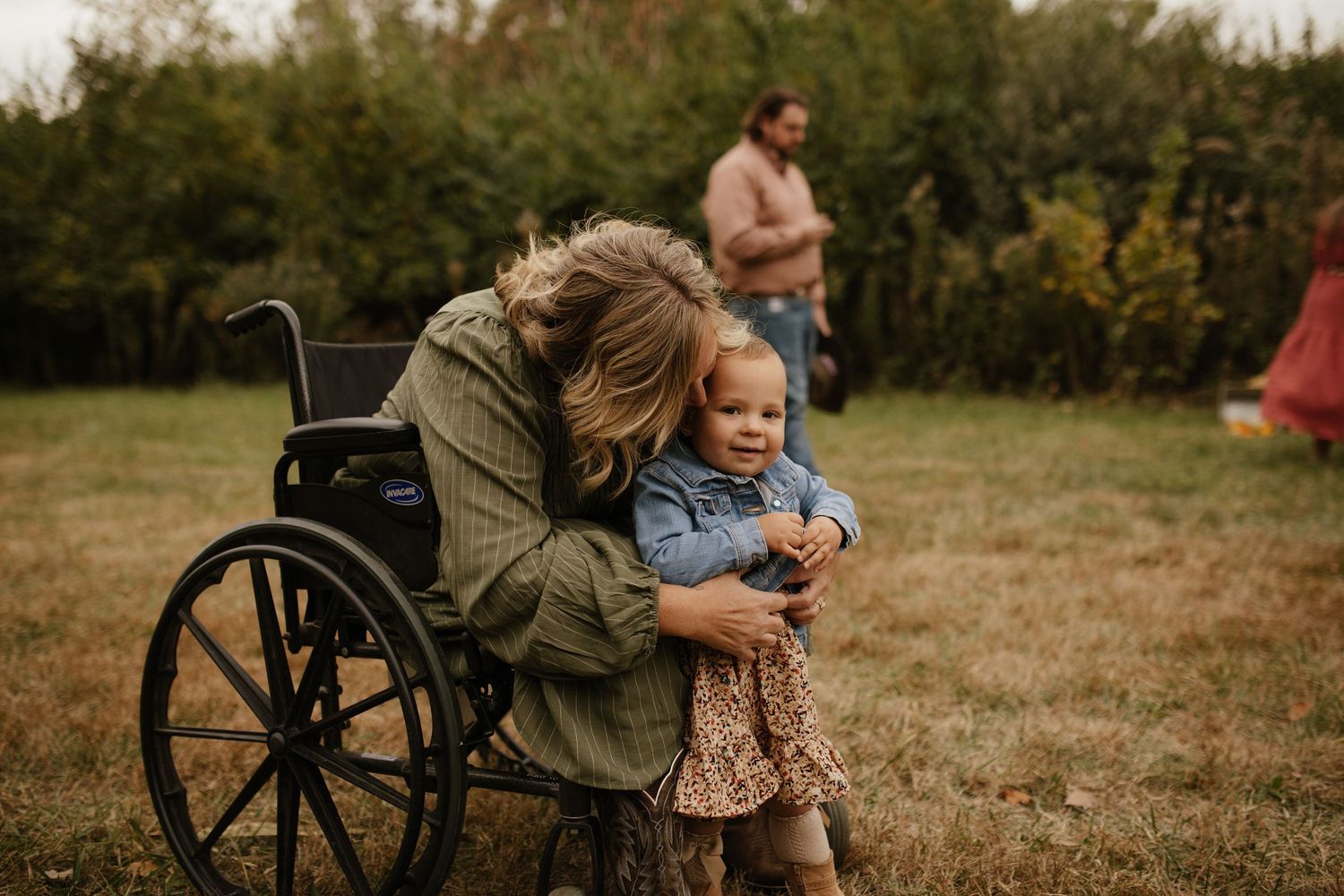 Tender family moments shared outdoors with wheelchair visible in natural setting.