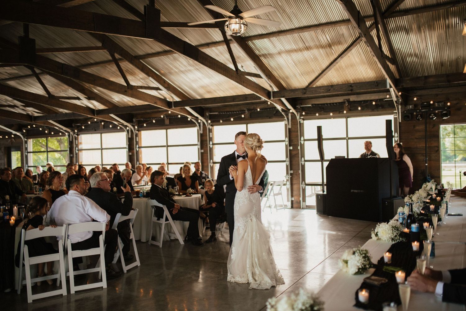 Indoor wedding reception space with string lights and rustic barn architecture.