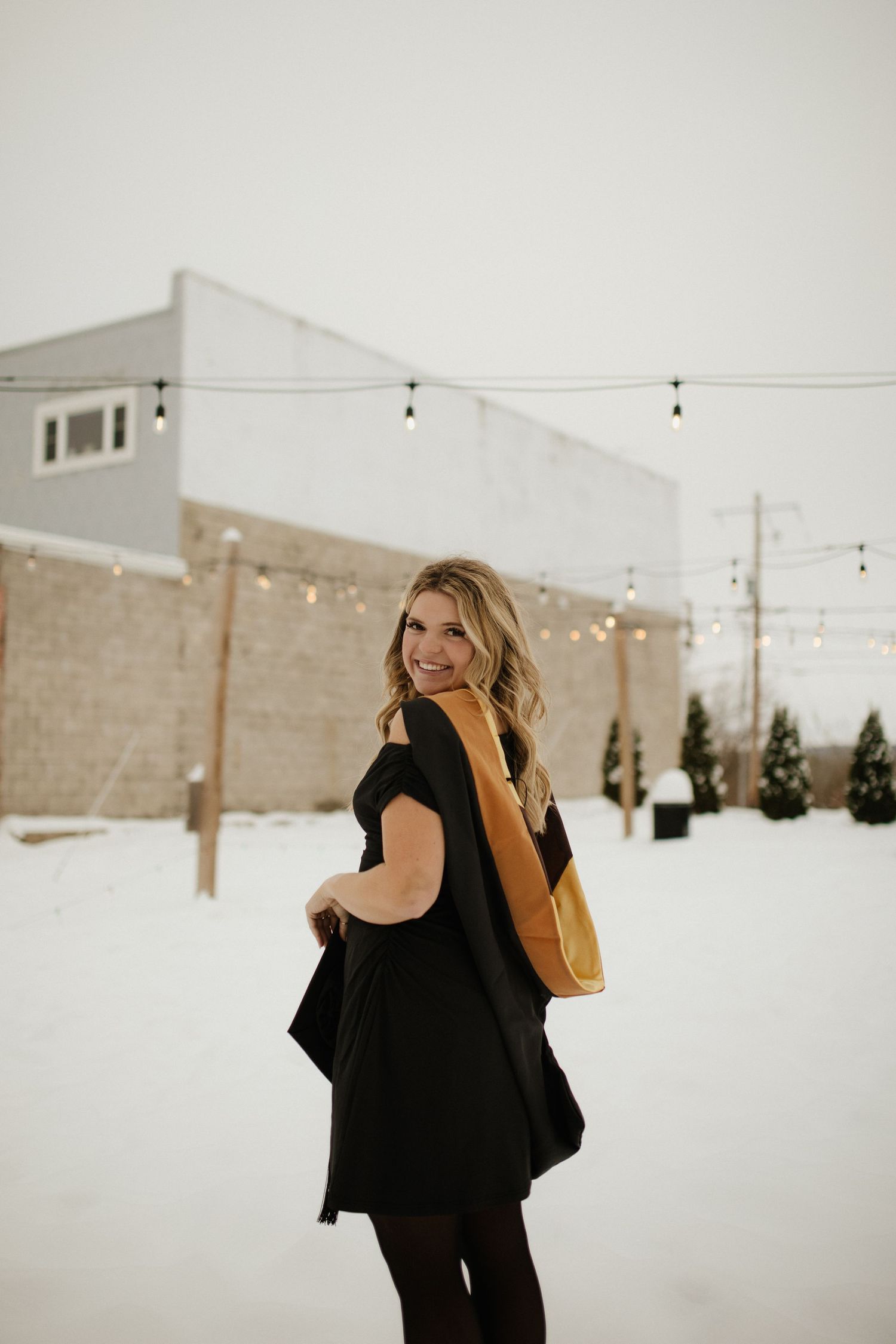Winter graduation photo with string lights and snow covered ground.