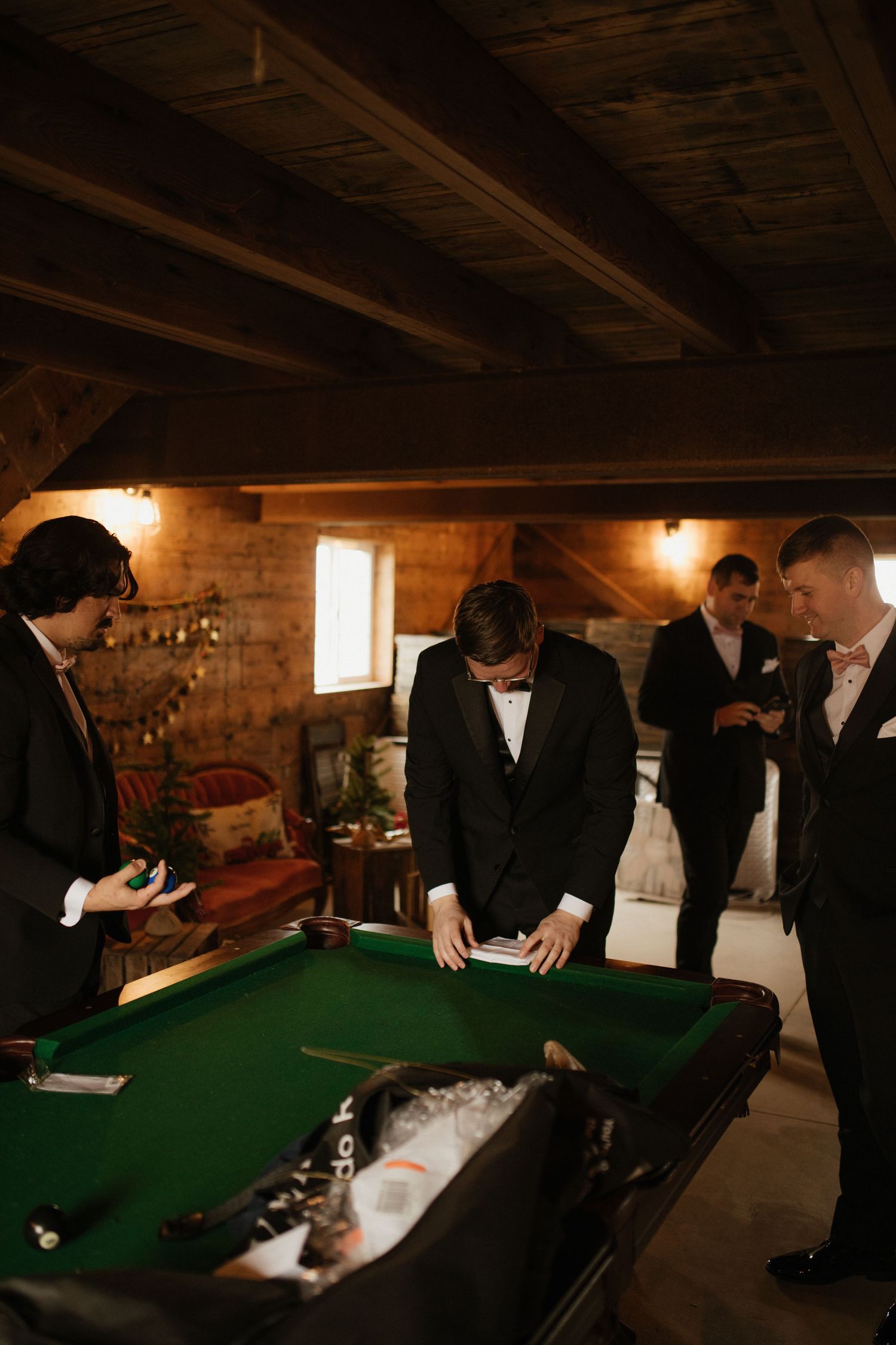 Wedding party gathered around green pool table in rustic basement setting.