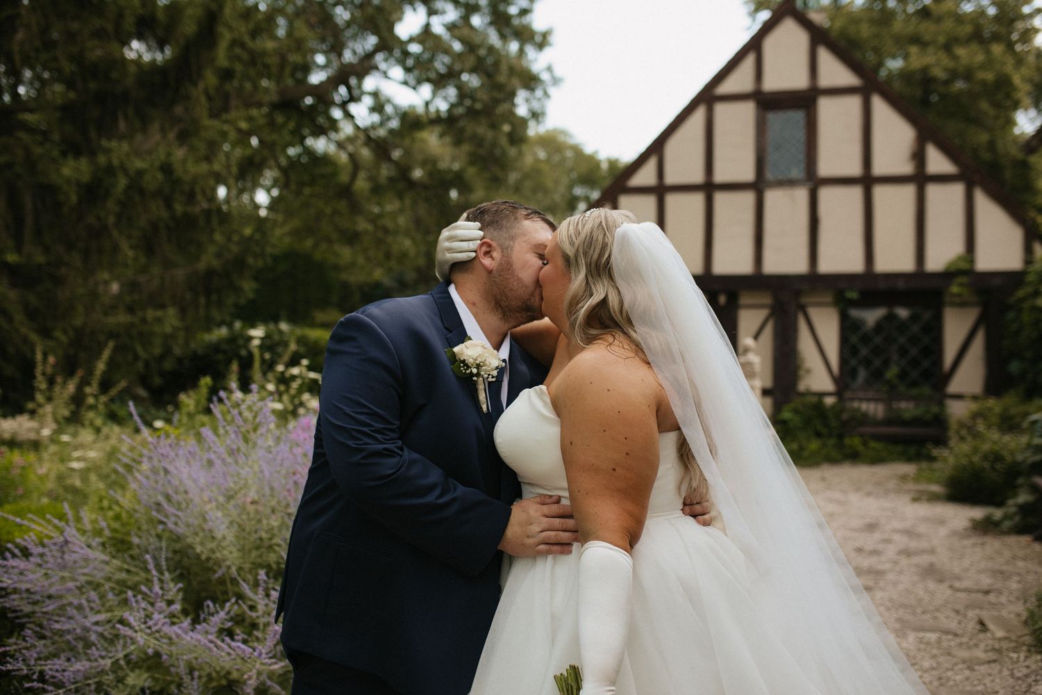 A tender moment captured between a couple in formal attire outside a Tudor-style building.