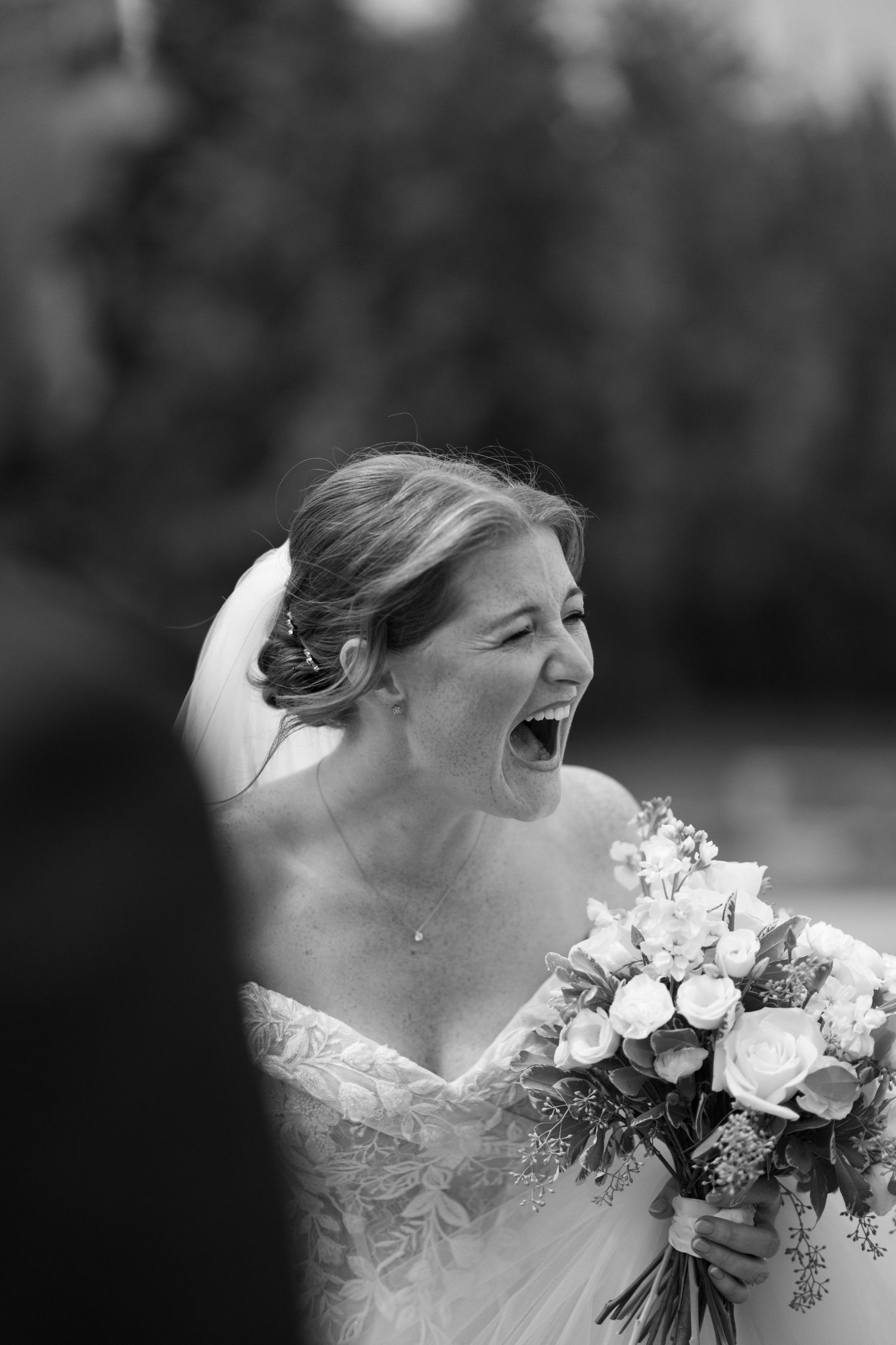 A joyful moment captured in black and white as a bride laughs while holding a beautiful bouquet of white roses.