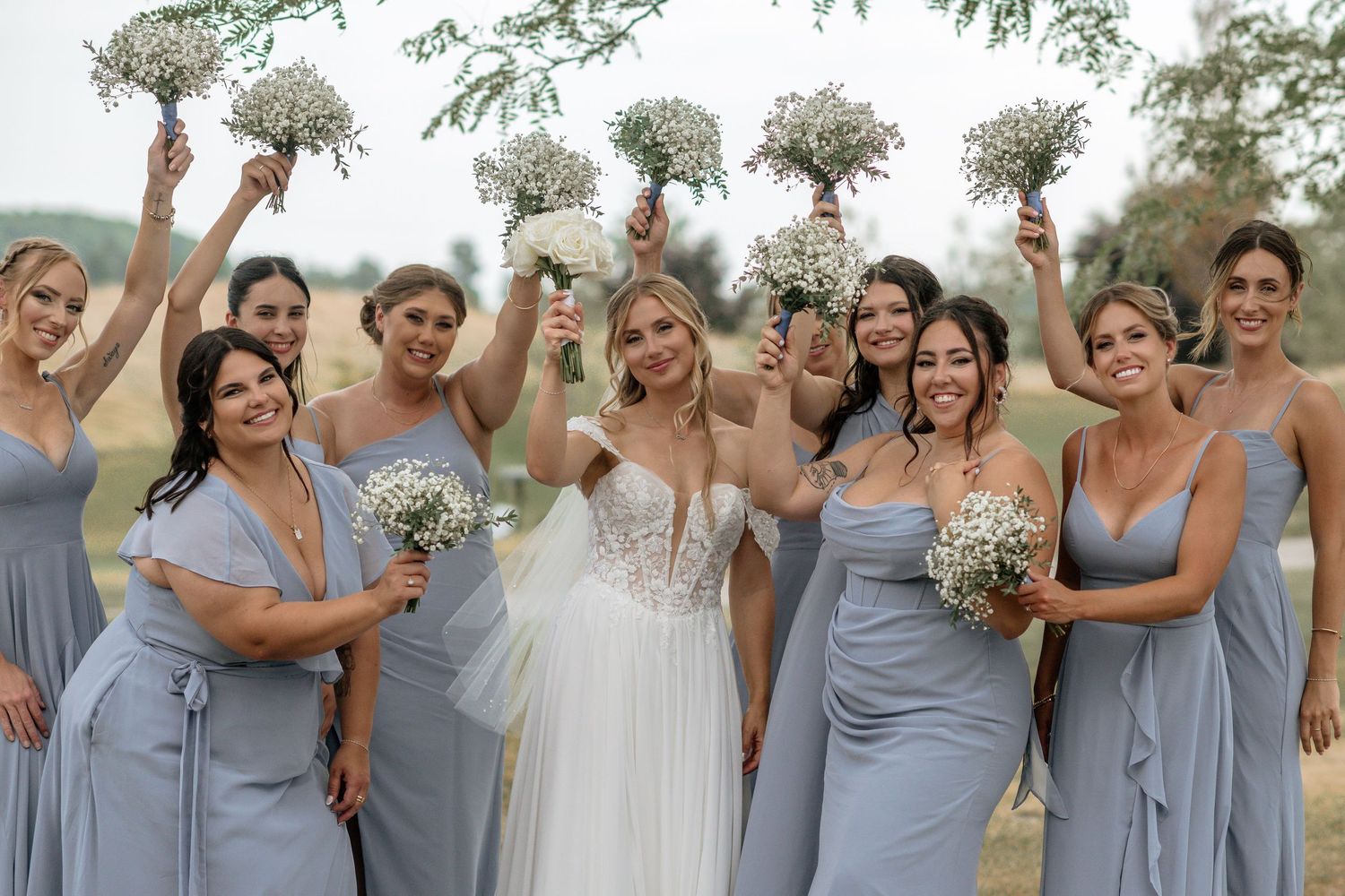 Bridesmaids in light blue dresses celebrate joyfully outdoors.