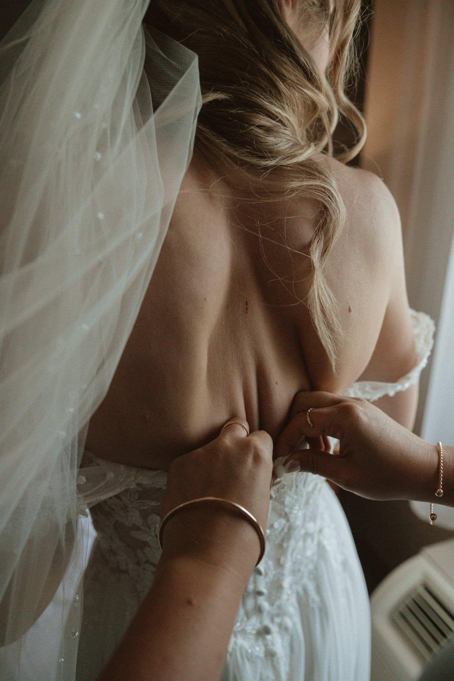 Close-up of hands fastening a white lace wedding dress.