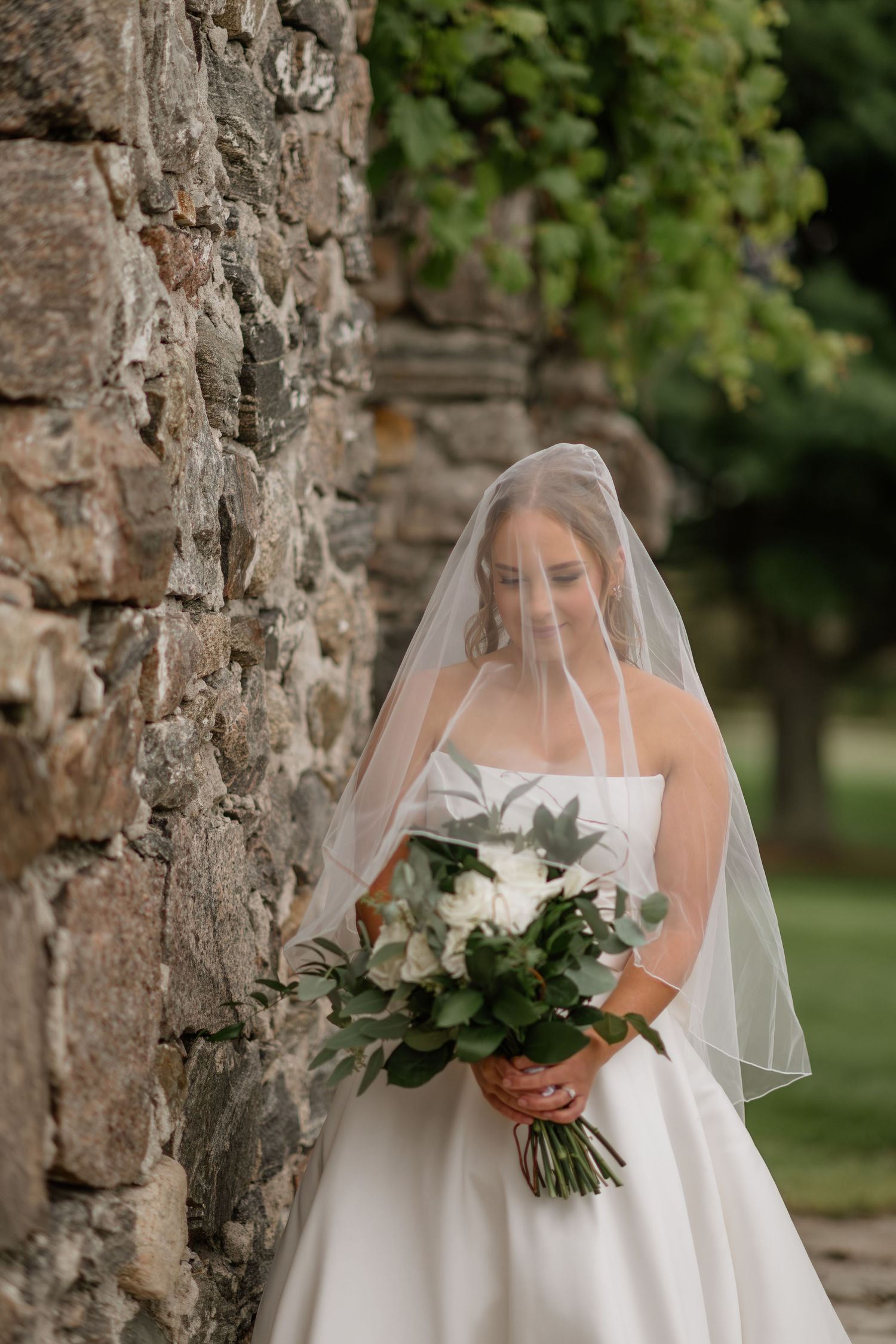 Classic bridal portrait against stone wall with white bouquet and flowing veil.