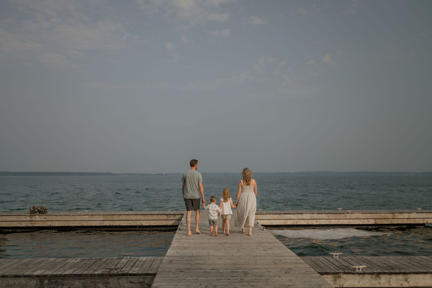 Family silhouettes walking together on a wooden pier by the ocean at dusk.