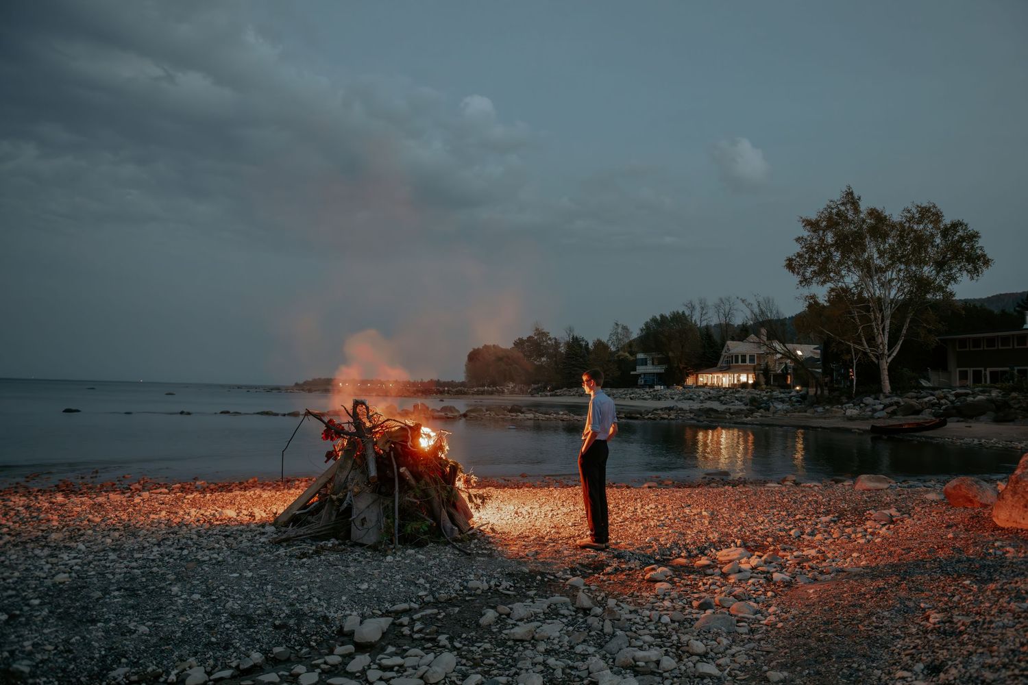 Multiple bonfires illuminate a dark beach at dusk creating a dramatic coastal scene.