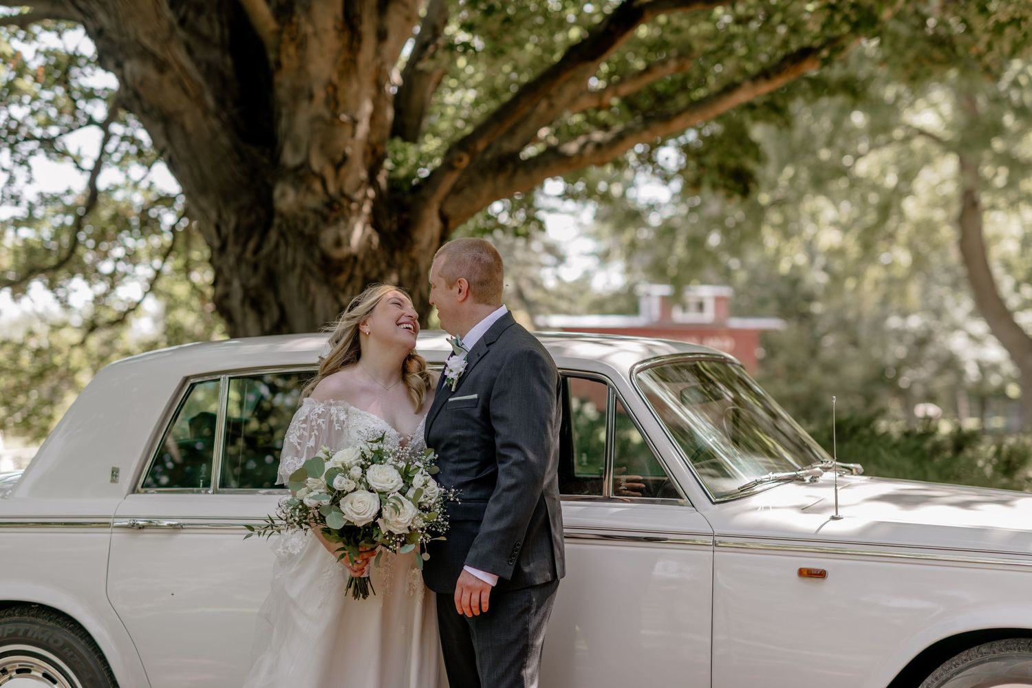 Romantic wedding couple shares tender moments in outdoor setting with vintage car and natural lighting.