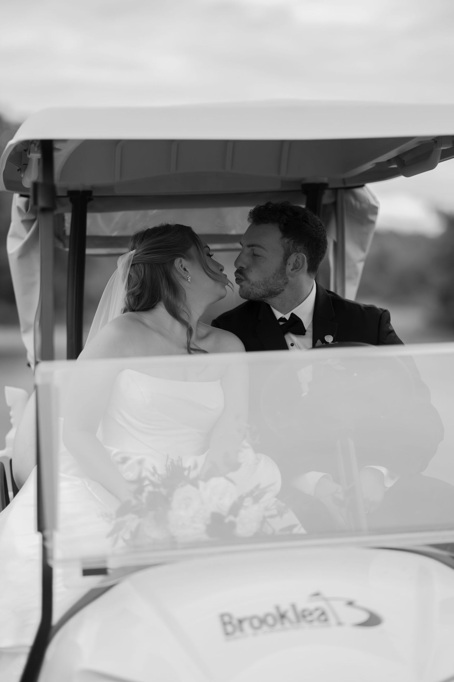 Black and white photo of newlyweds sharing intimate moment in golf cart.