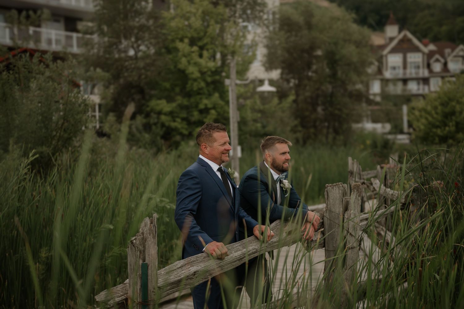 A couple walks together through a lush garden path with rustic wooden fencing and greenery.