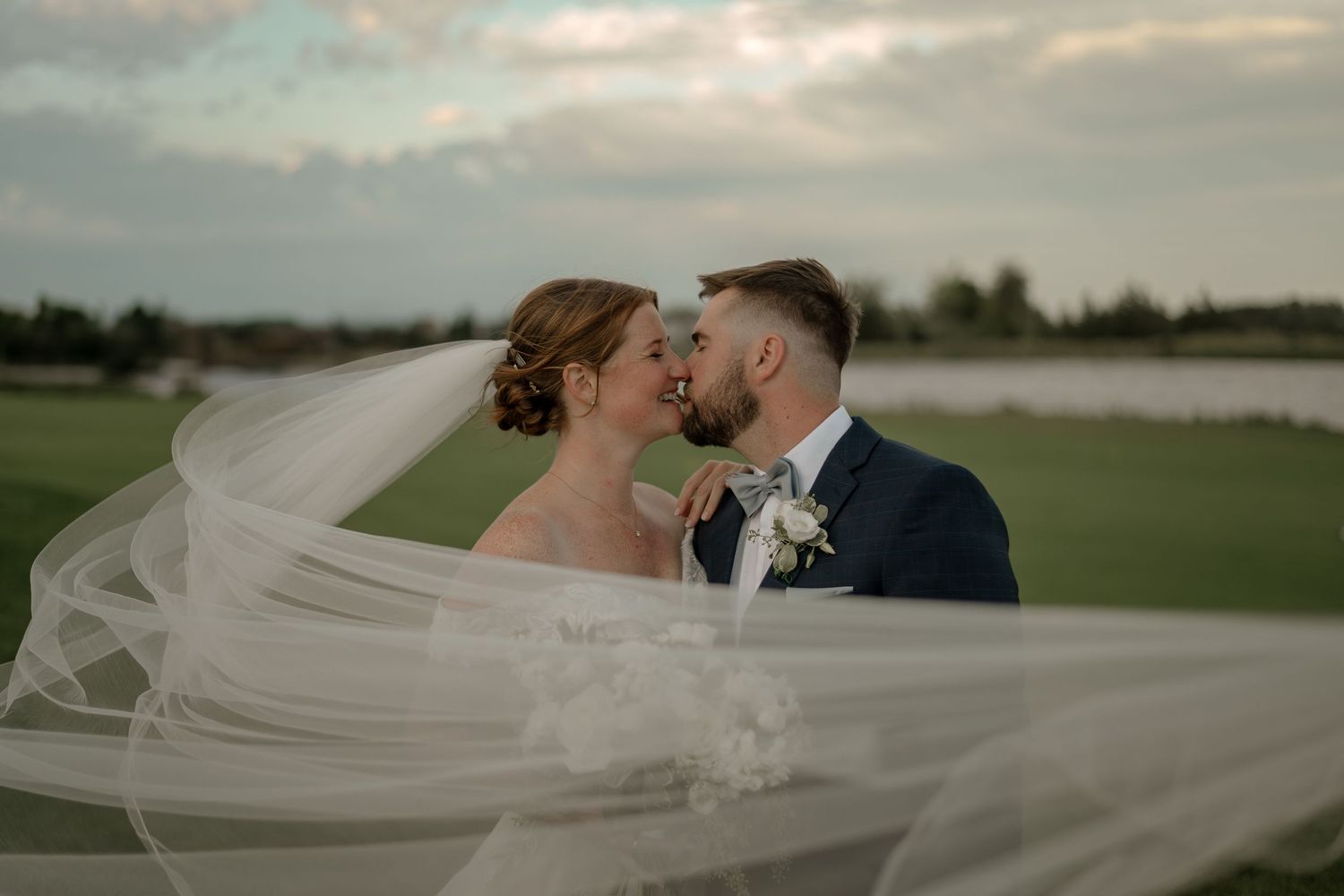 A flowing white wedding veil catches the breeze during an outdoor beach ceremony at sunset.
