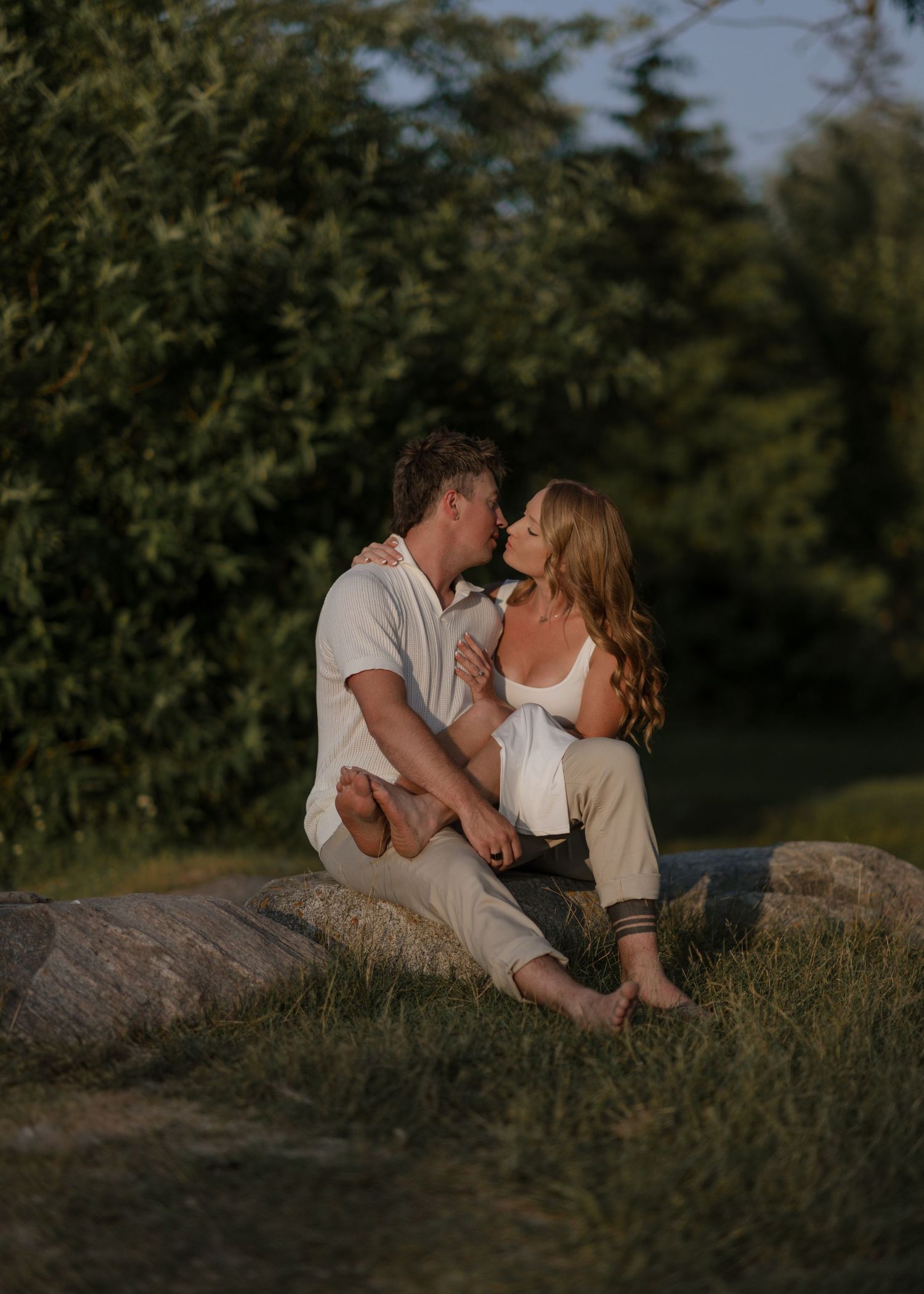 Couple shares romantic moments on rocky outcrop during sunset photoshoot.