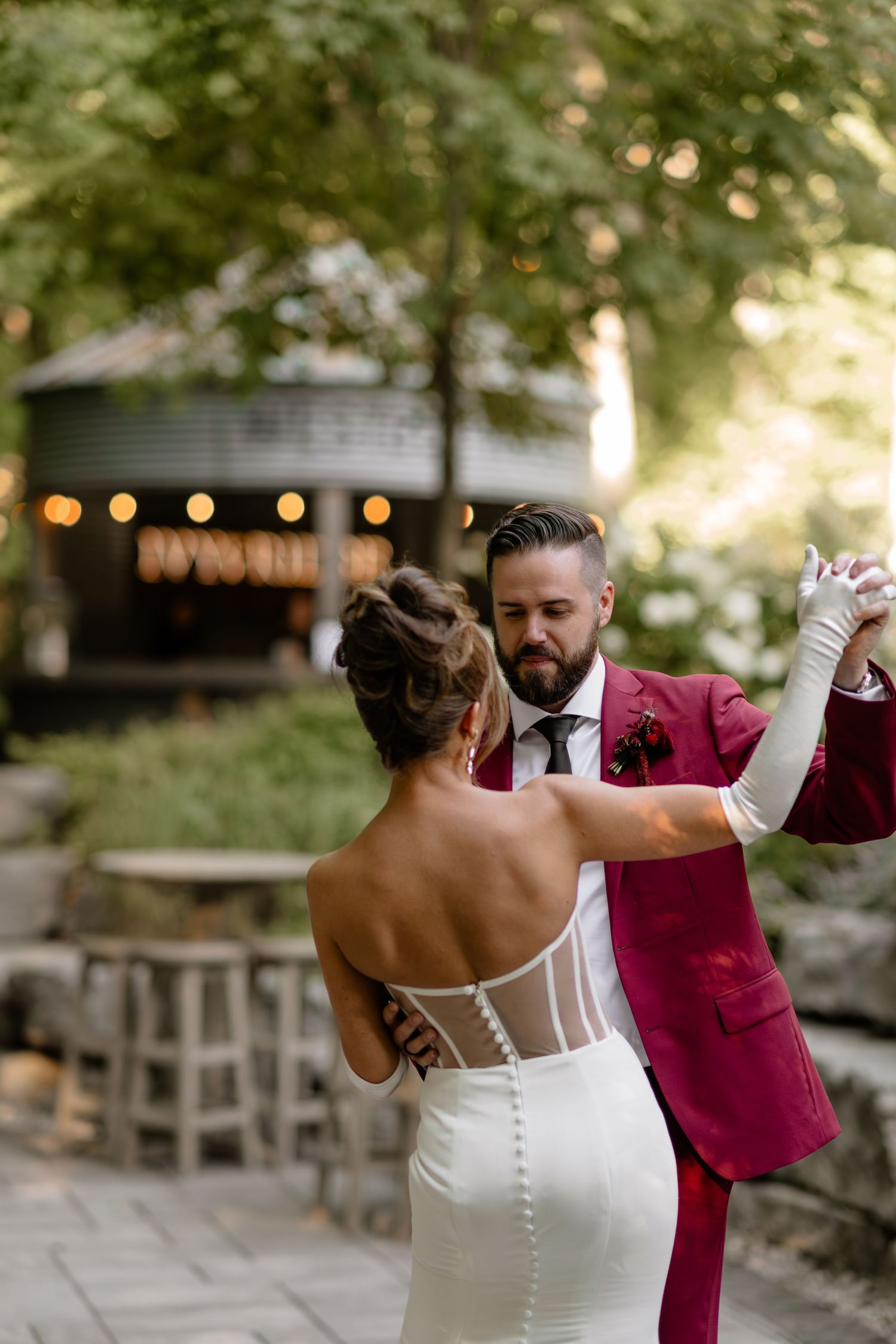 Newlyweds share a playful dance moment in burgundy and white attire.