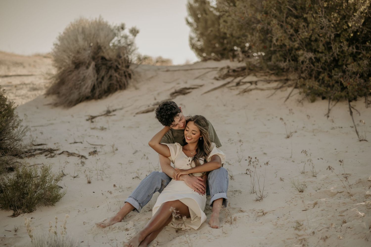 Two people share an intimate moment on sandy dunes during a desert photoshoot at golden hour.