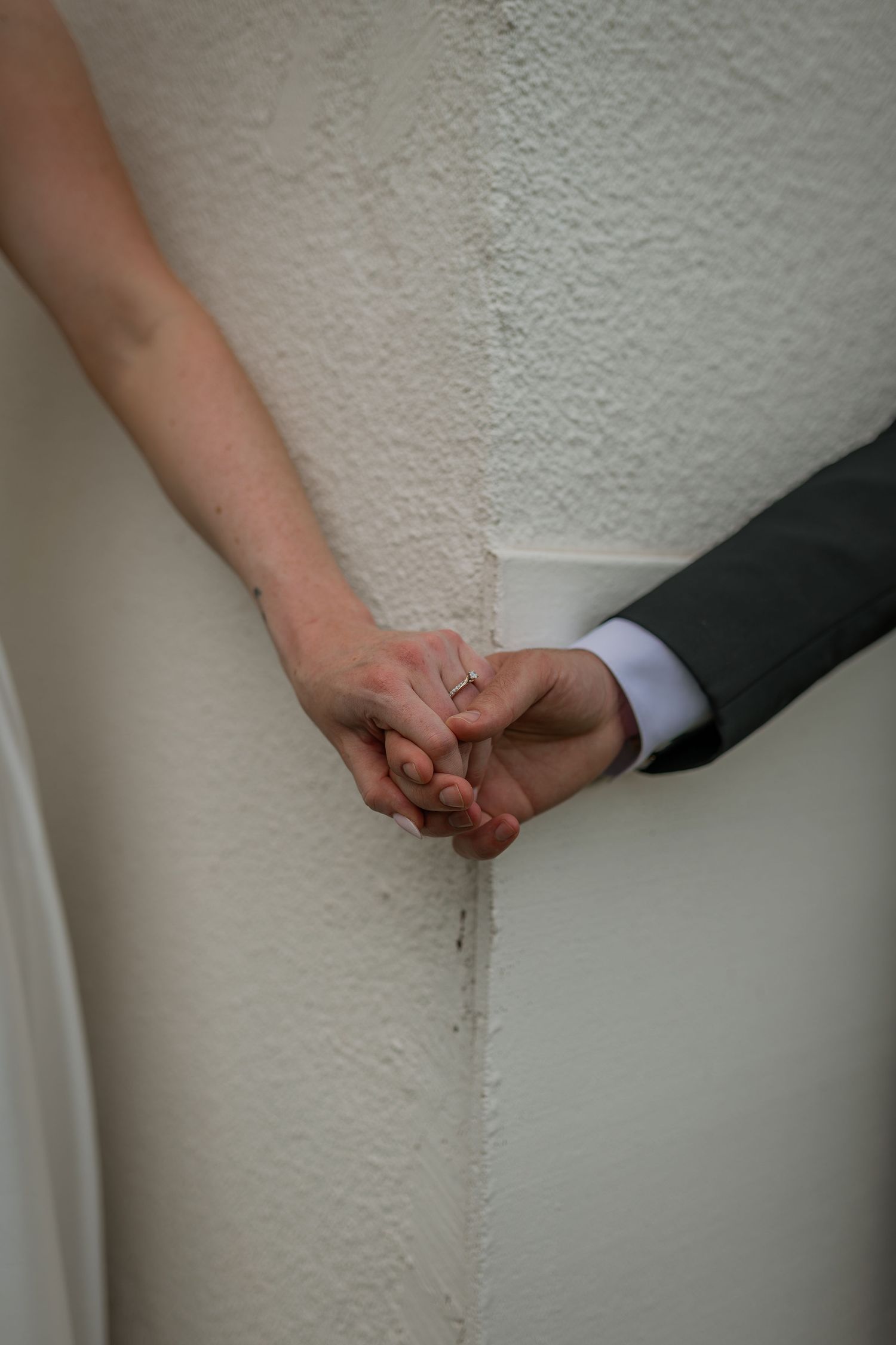 Close-up of hands holding each other against a white textured wall.