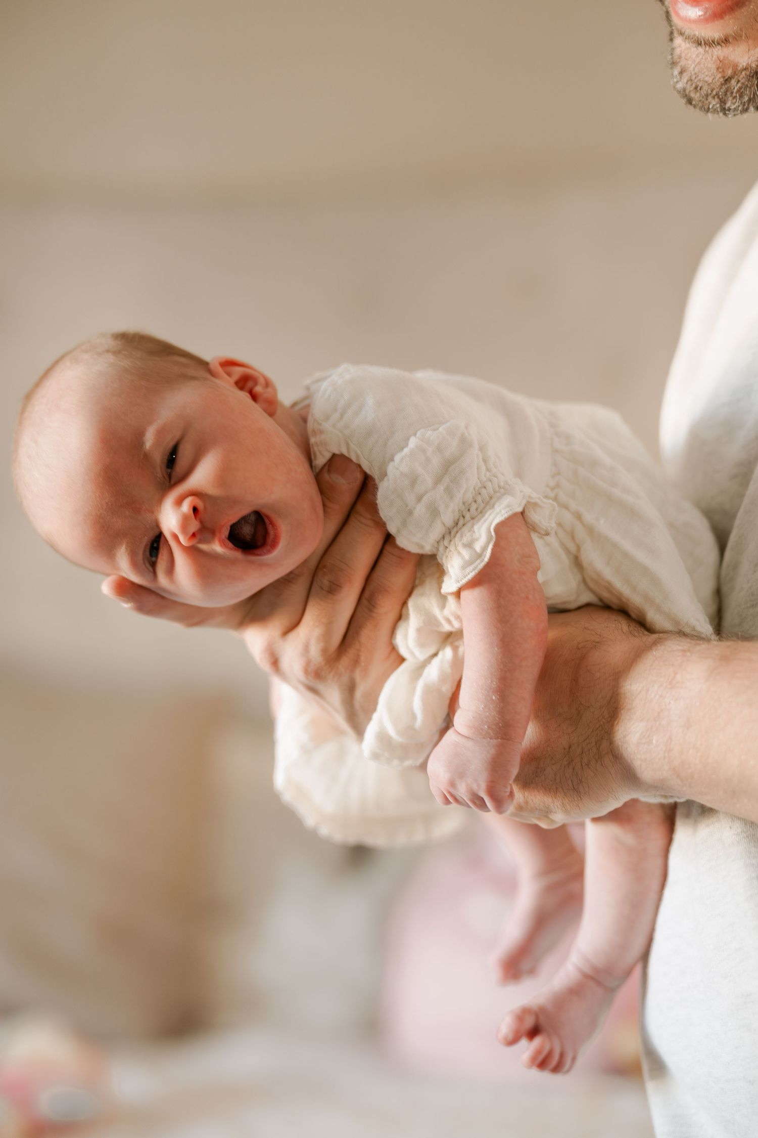 Newborn baby yawning while being held in soft natural light.