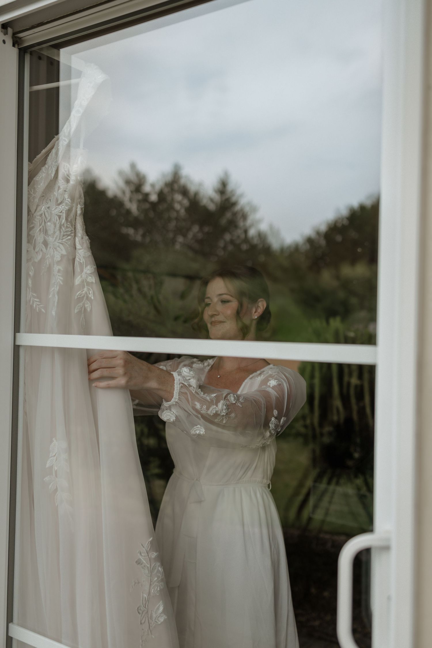 White wedding dress hanging in front of large windows with natural light.