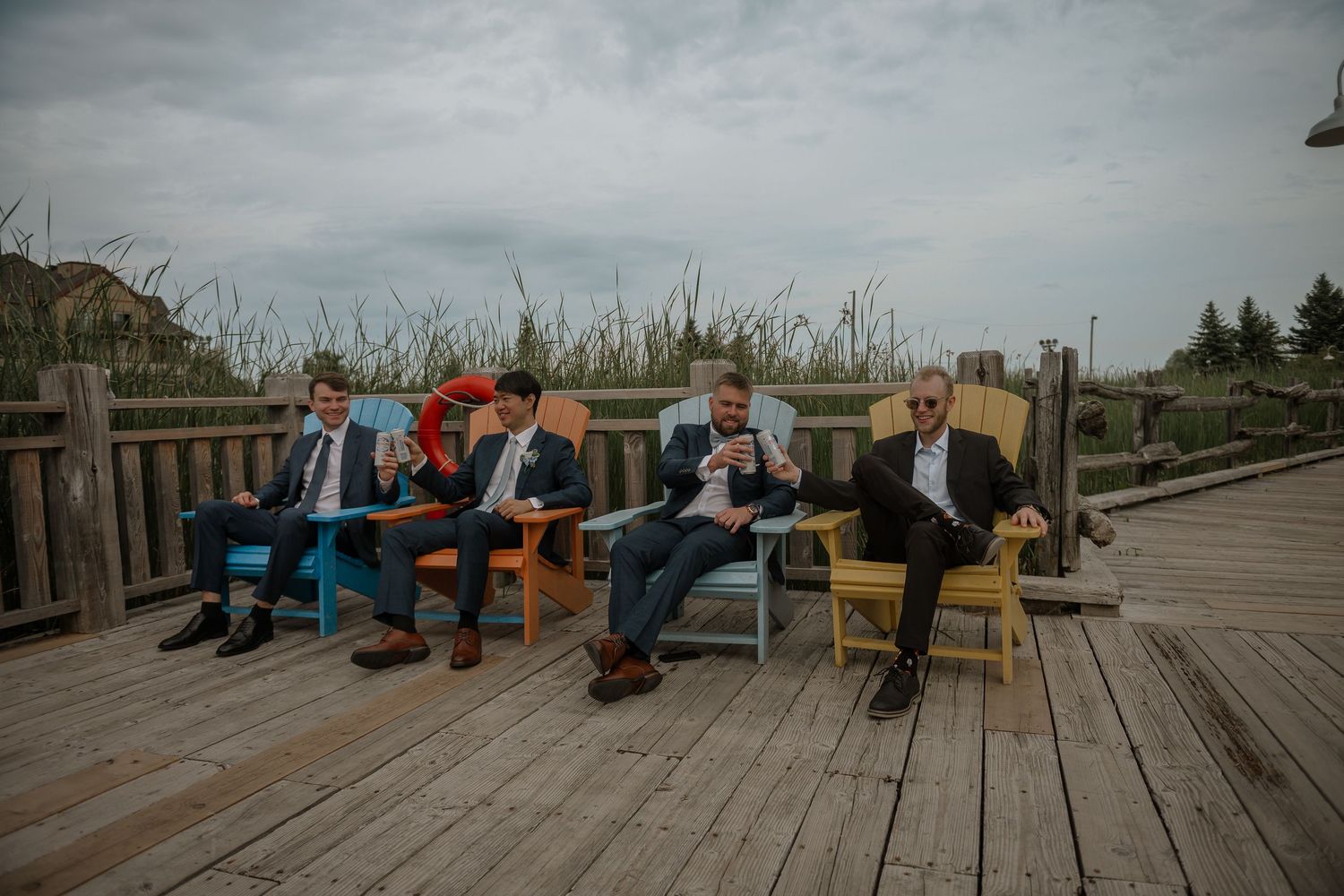 Weathered wooden boardwalk stretches along a coastal shoreline with colorful Adirondack chairs placed at intervals.