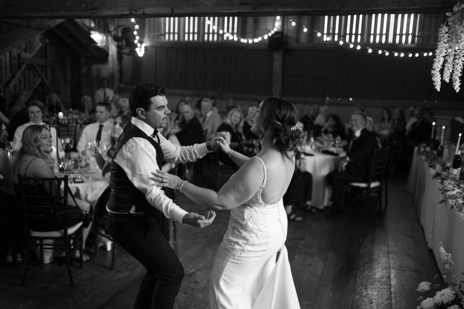 A couple performs a romantic dance at a wedding reception with string lights glowing in the background.