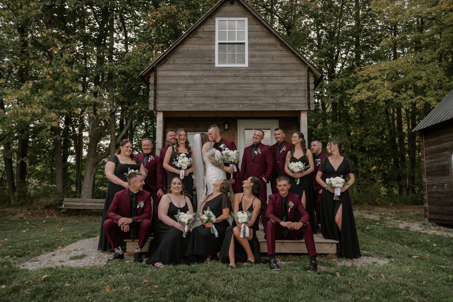 Rustic wooden barn serves as backdrop for wedding party photos in burgundy and white.
