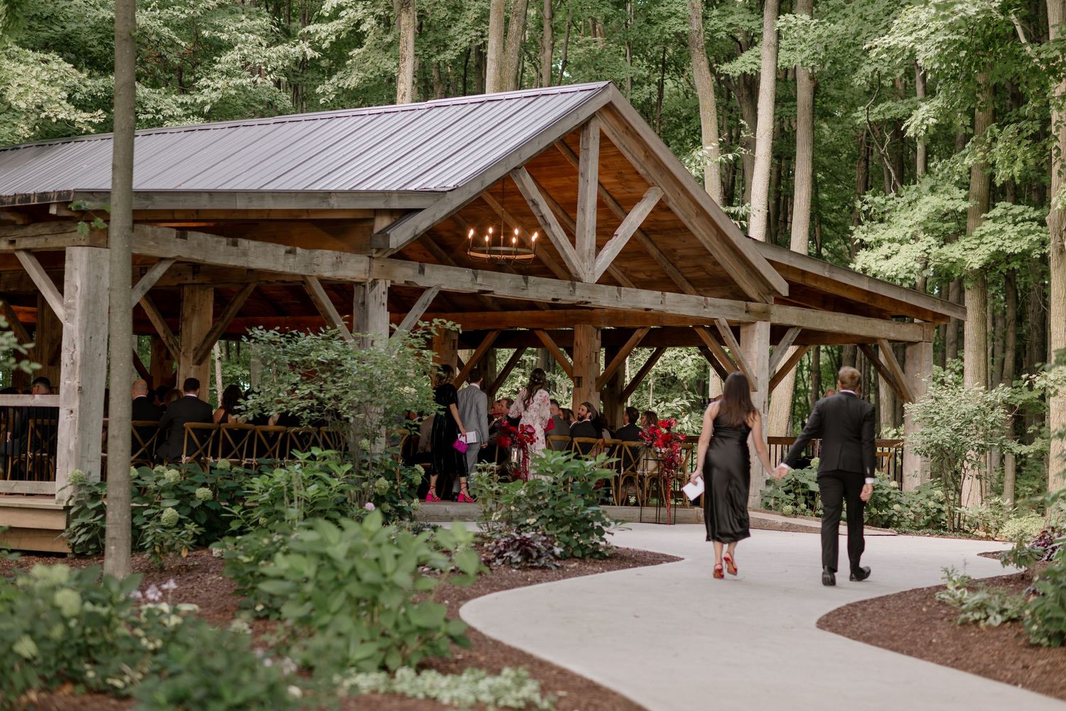 Rustic wooden pavilion surrounded by lush forest greenery with guests gathering.