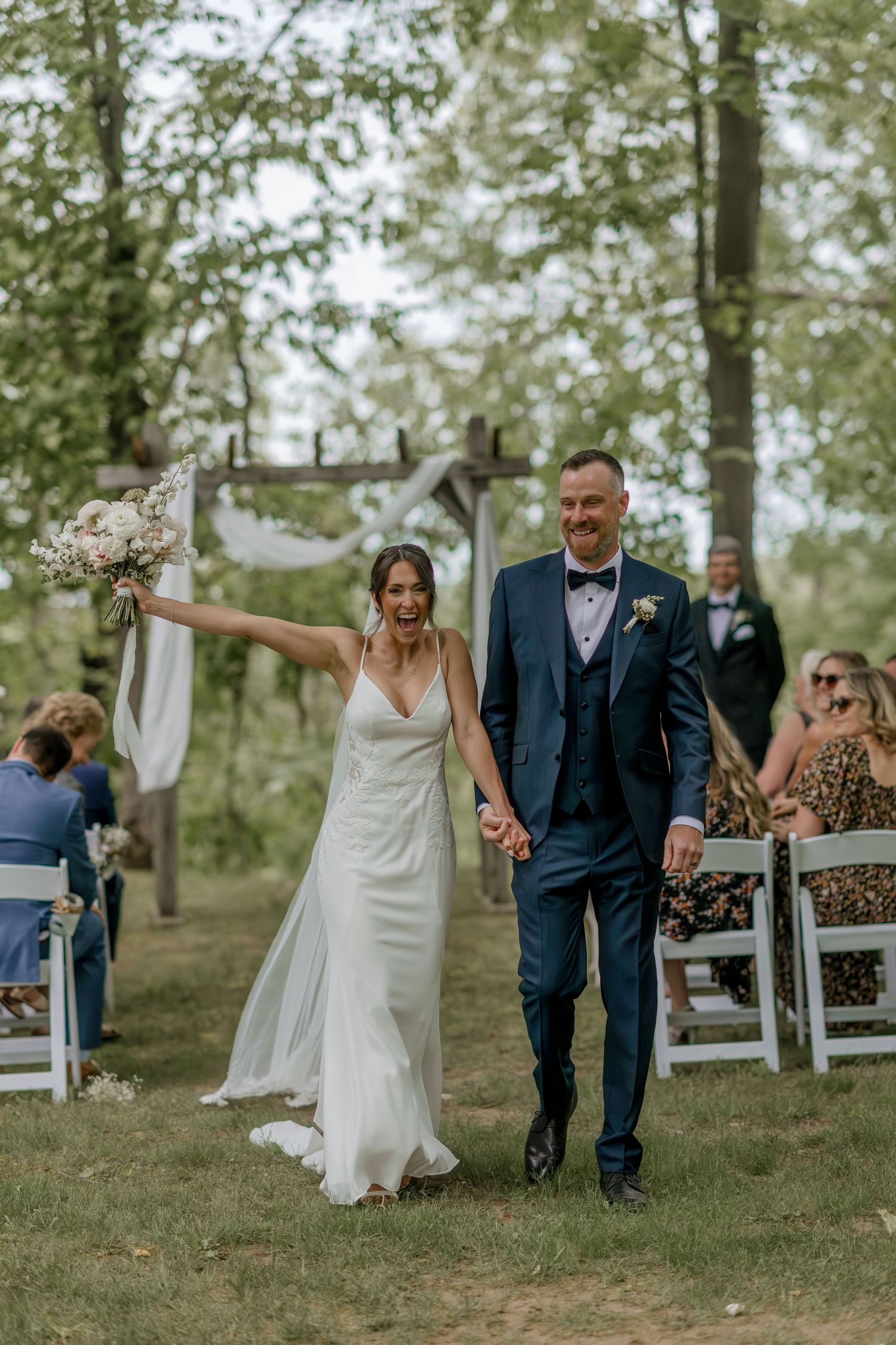 Joyful wedding celebration with guests in an outdoor woodland setting.