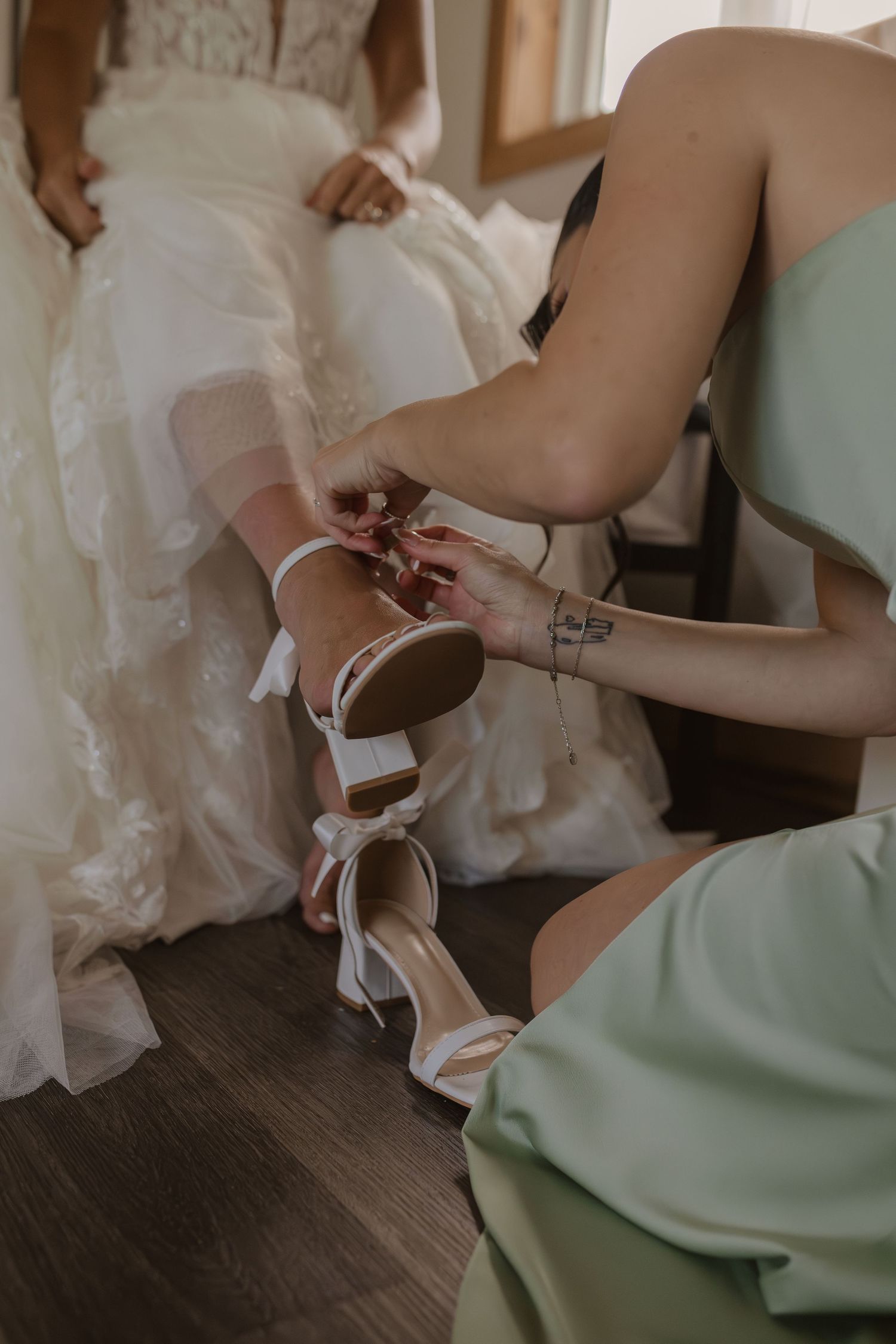 Detail shot of someone helping with wedding shoes during bridal preparation.
