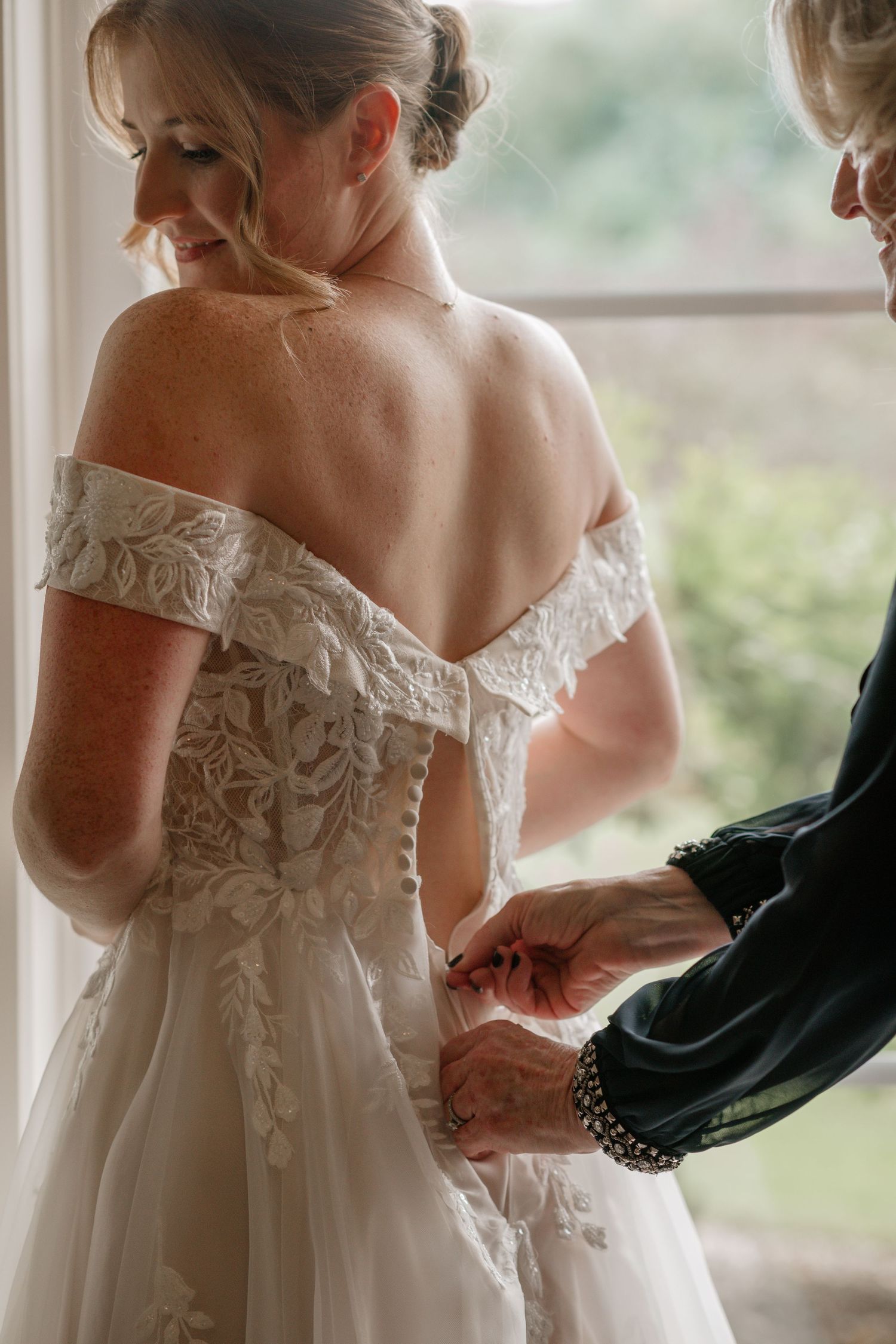 Close-up details of a white lace wedding dress being buttoned.