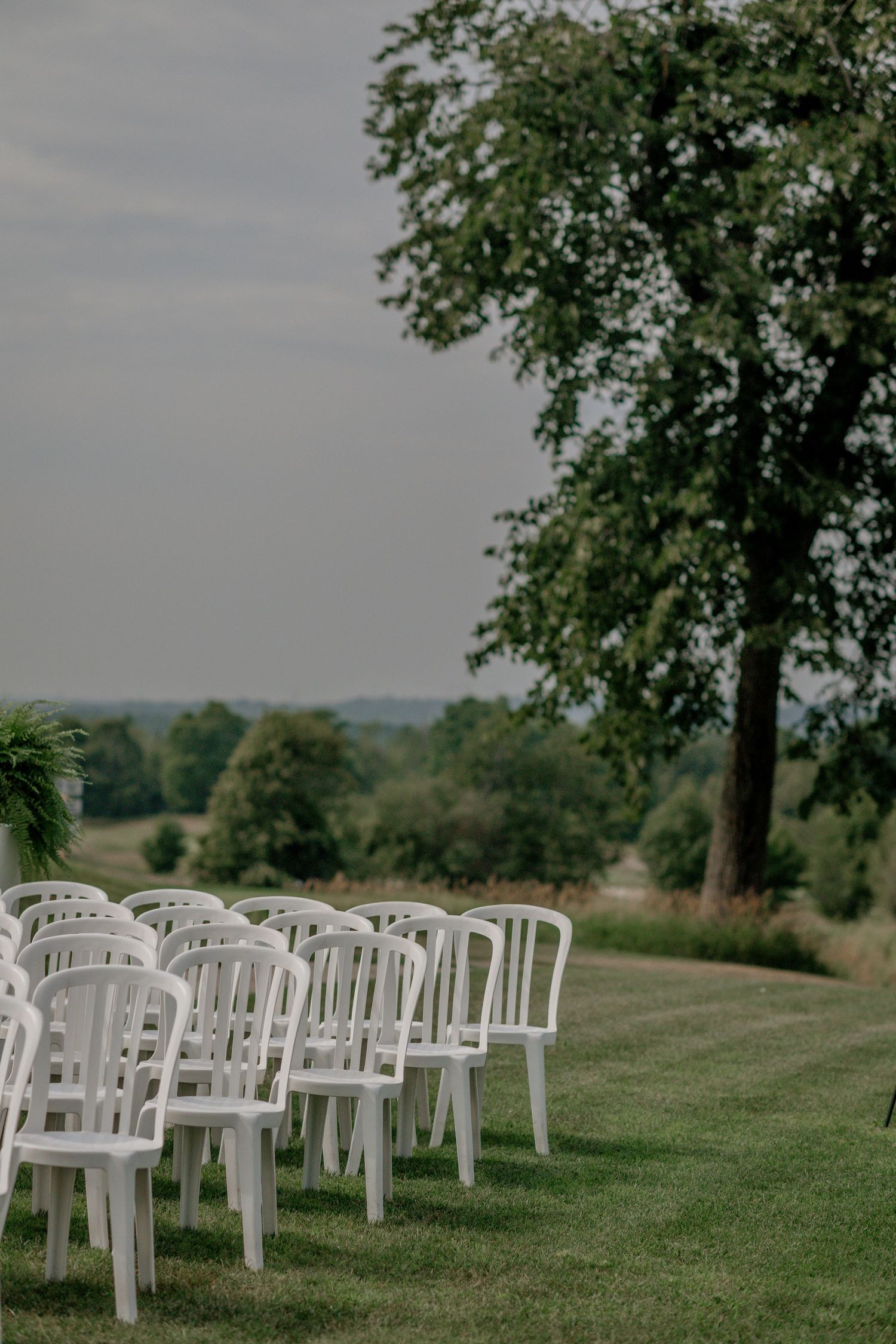 White plastic chairs arranged in rows on a grassy hillside for an outdoor wedding ceremony.
