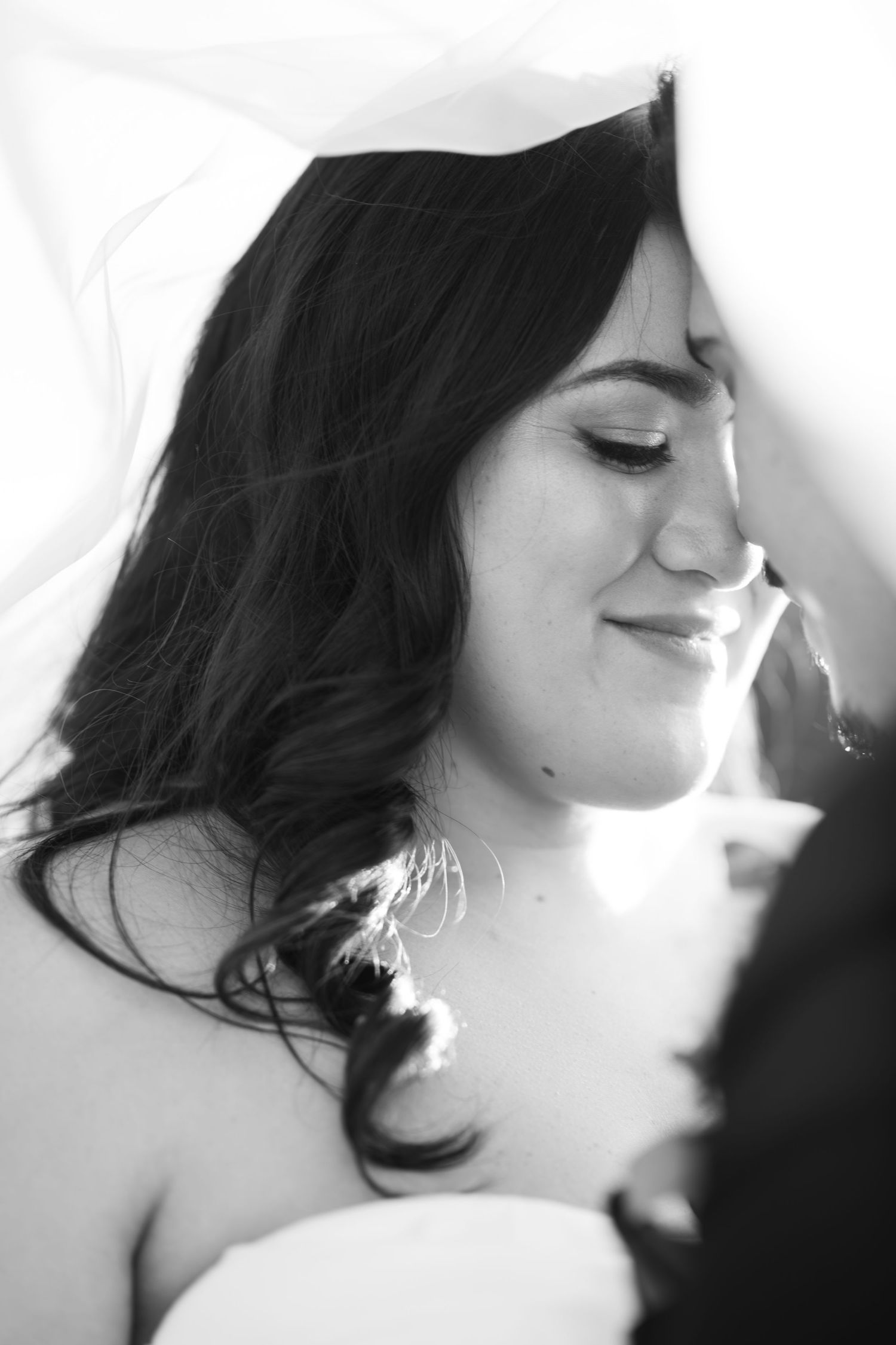 Black and white portrait of a serene woman with dark wavy hair and closed eyes in soft lighting.