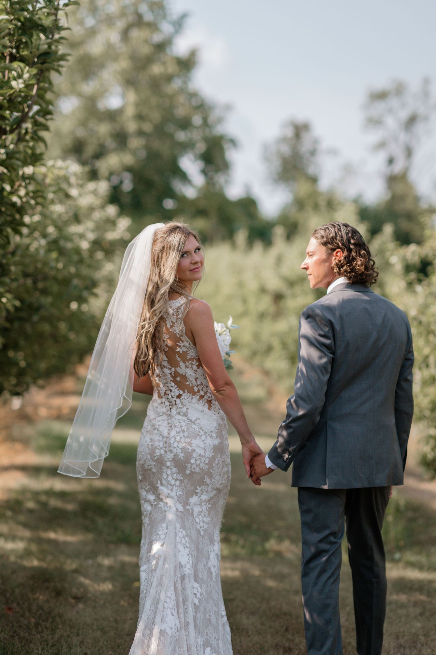 Newlyweds walking together through an orchard on their wedding day.