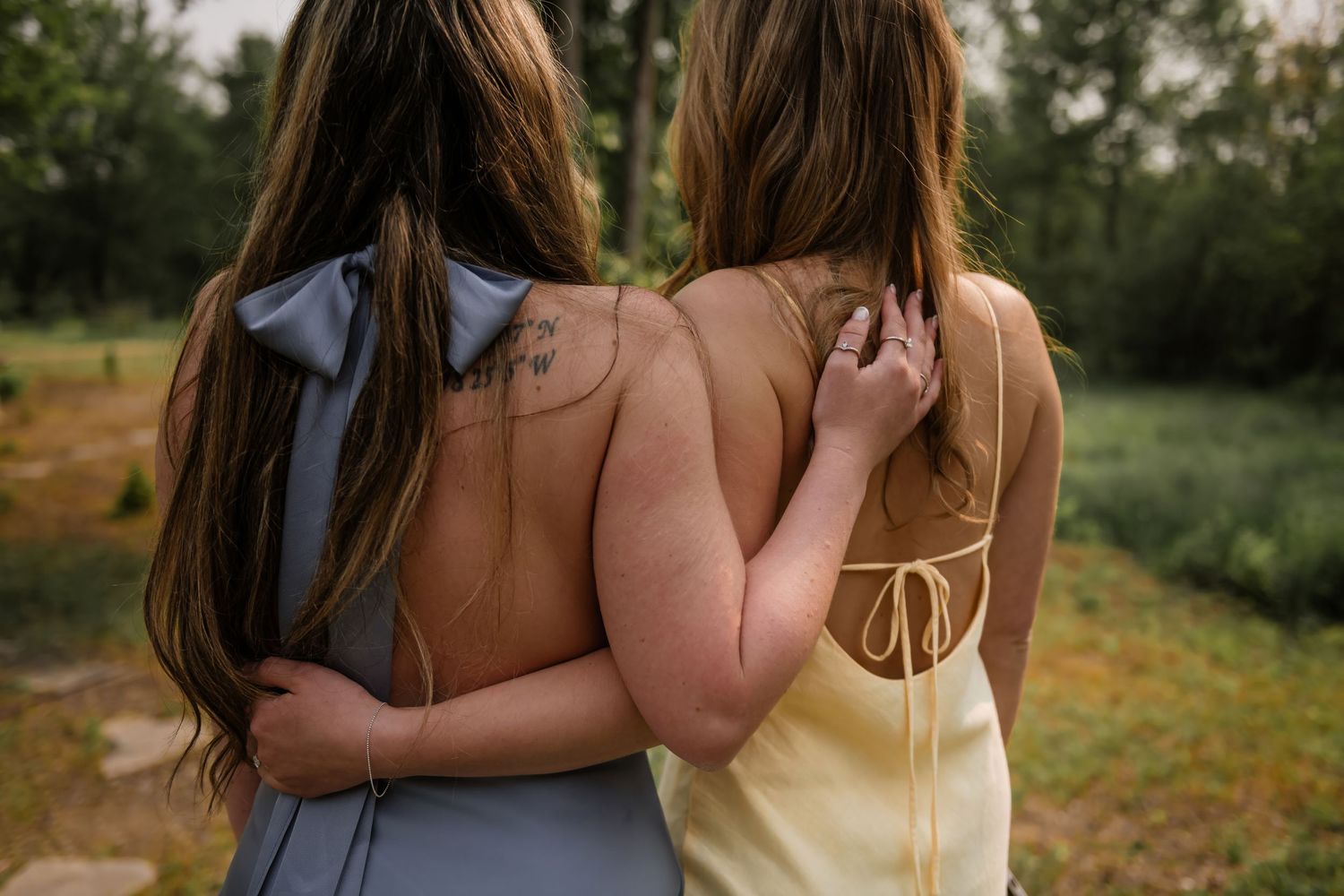 Two people in brown dresses walking together through a lush green field at sunset.