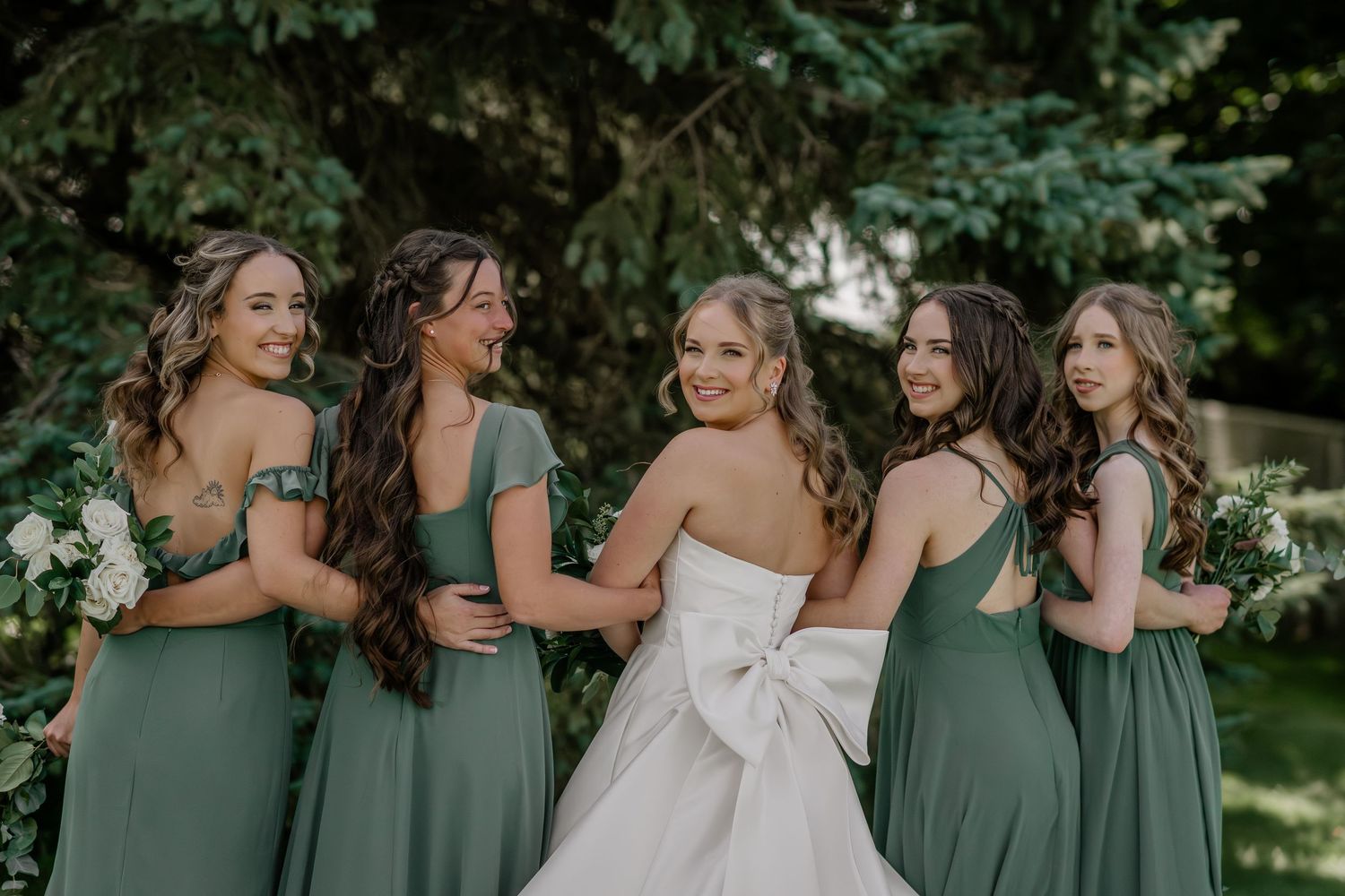 Wedding party in sage green dresses poses together outdoors.
