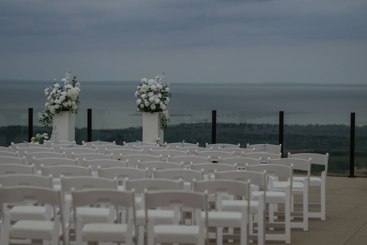 White chairs arranged on a beach deck for an oceanfront wedding ceremony with floral decorations.